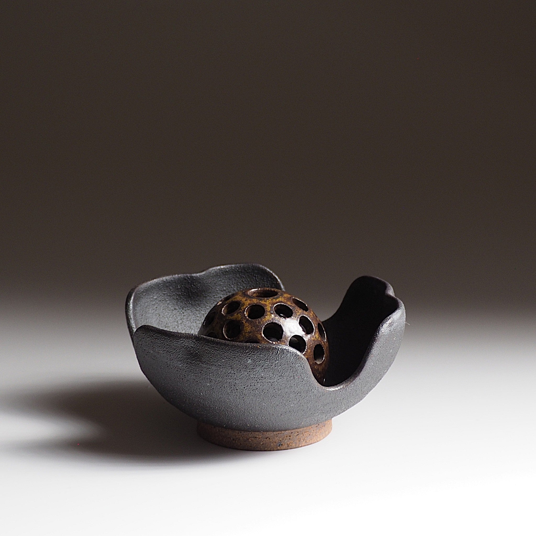 Front view of a black ceramic flower frog against a dark, faded background. Tsukushi