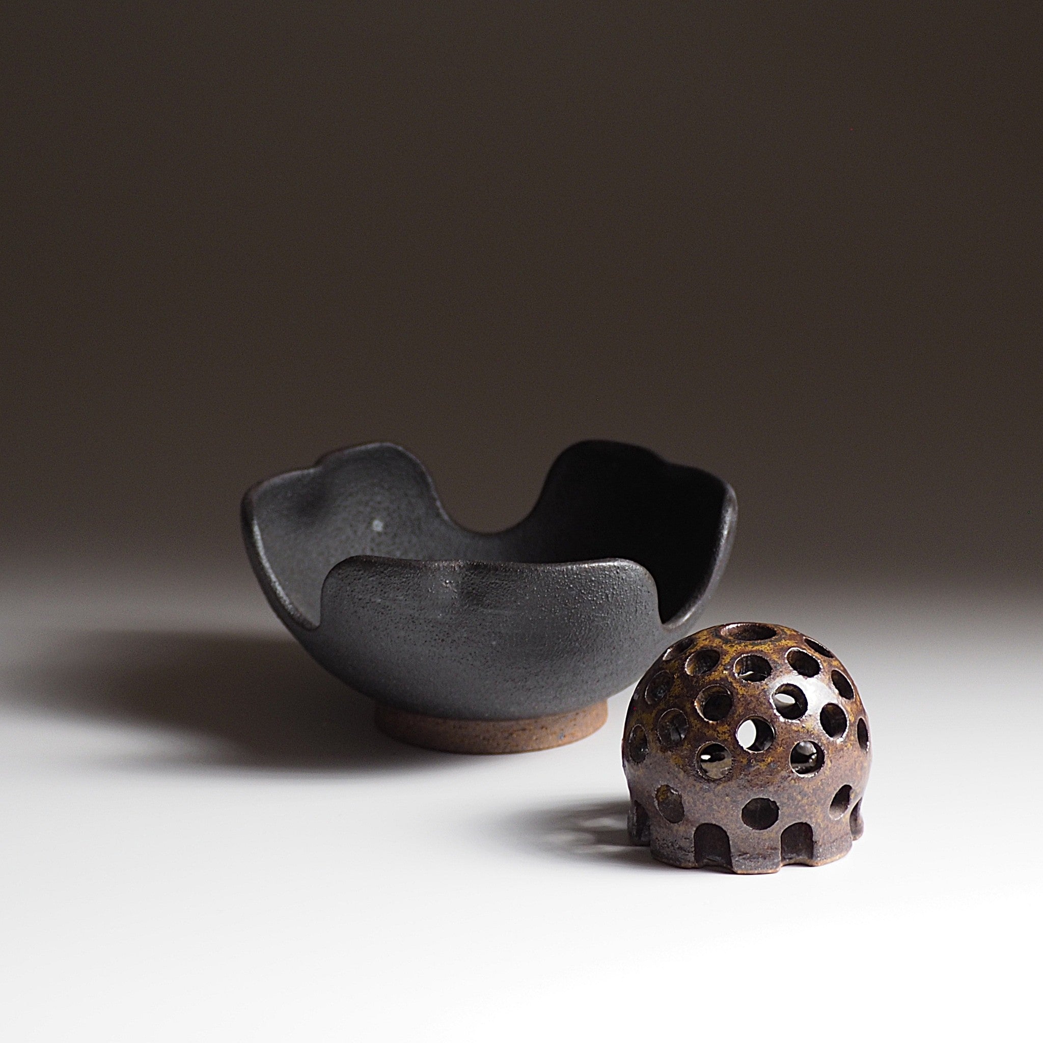 Japanese ceramic flower frog and matching bowl against a dark, faded background. Tsukushi