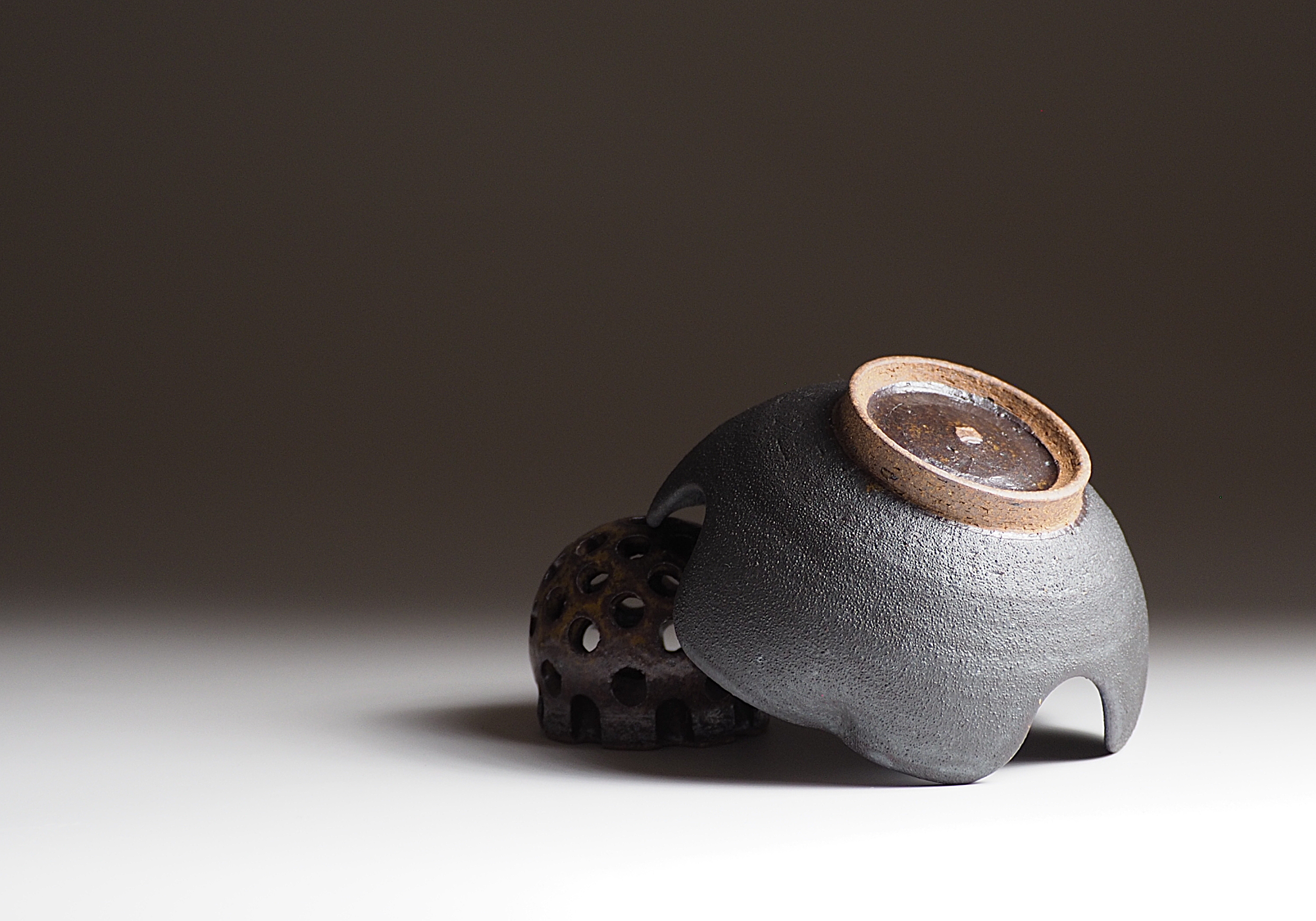 Bottom view of a Japanese ceramic bowl in black lying diagonally on a ceramic flower frog. Tsukushi.