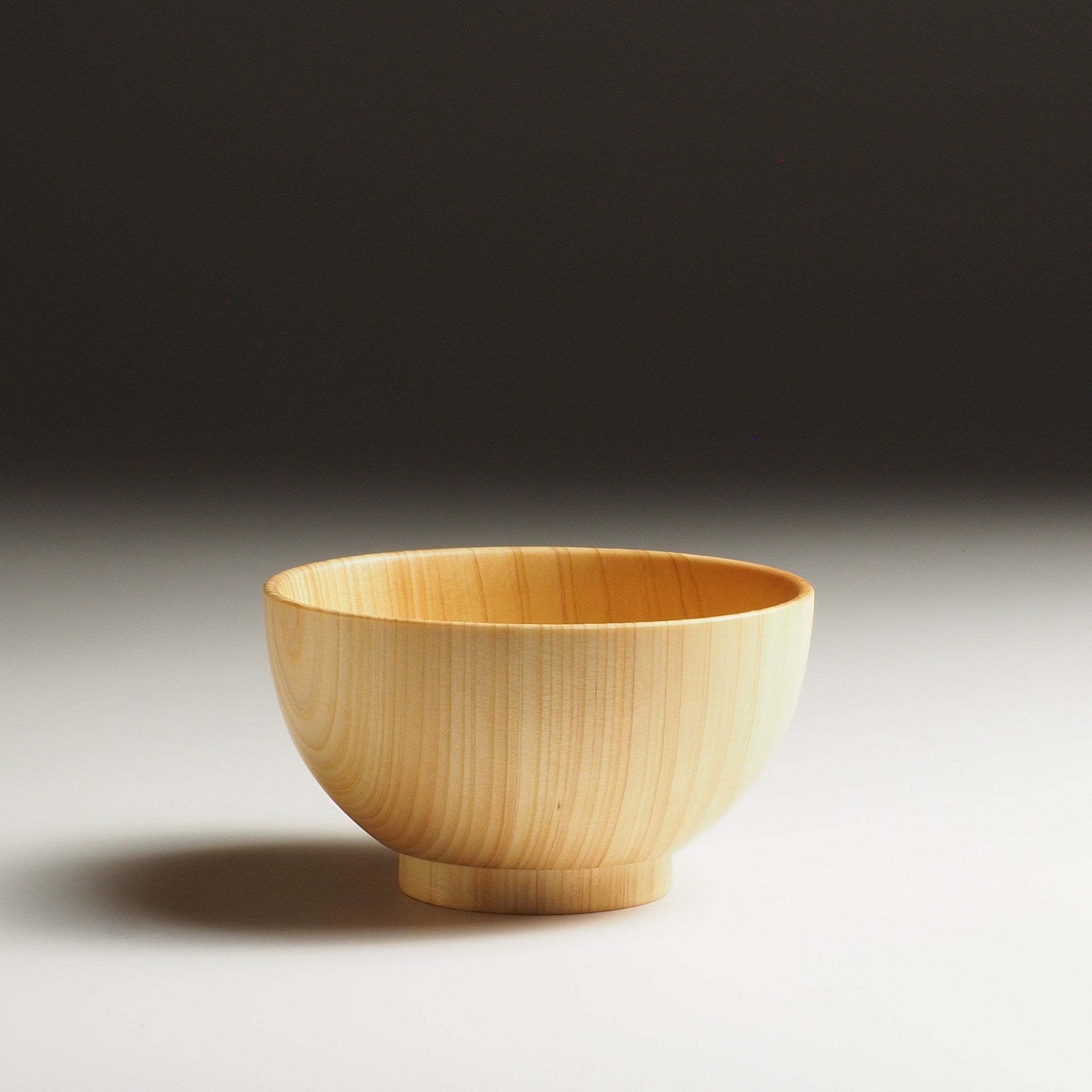 A side view of a Japanese wooden macha tea bowl on a beige background. Tsukushi