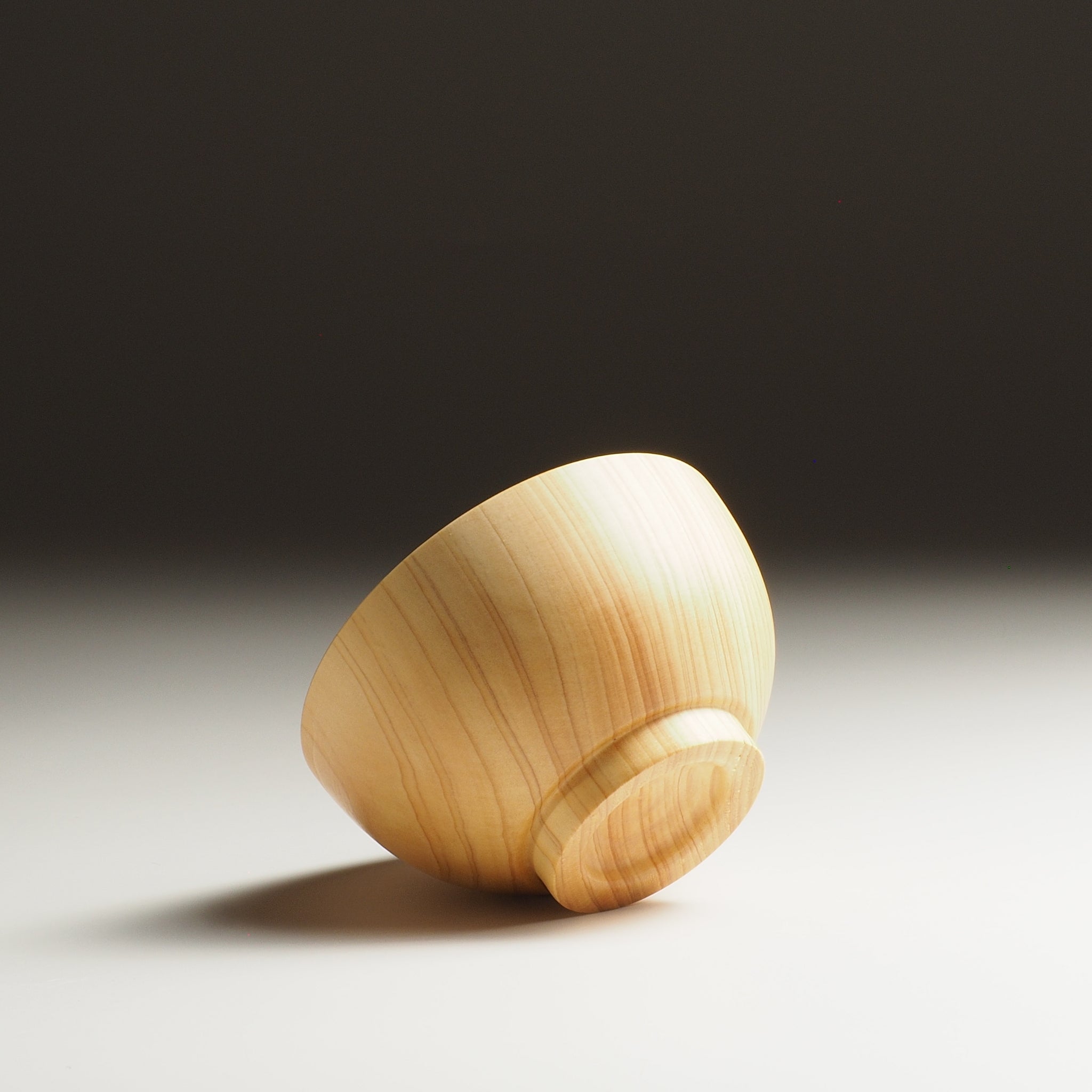 A bottom view of a Japanese wooden macha tea bowl on a beige background. Tsukushi