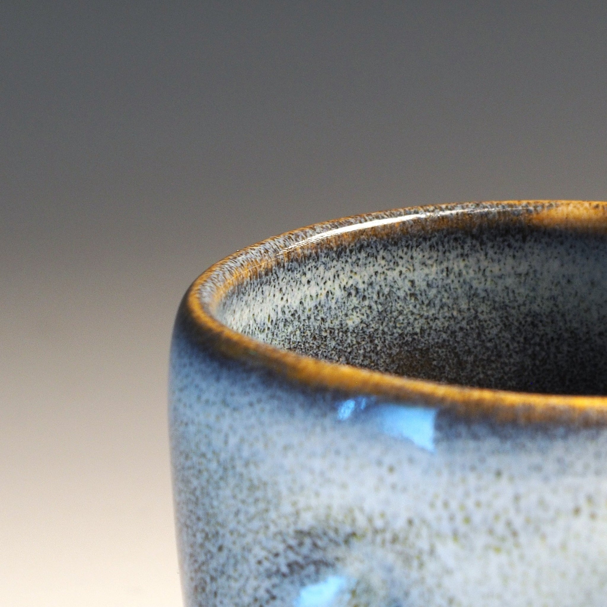Close-up of a Japanese ceramic teacup with speckled glaze on a gradient background