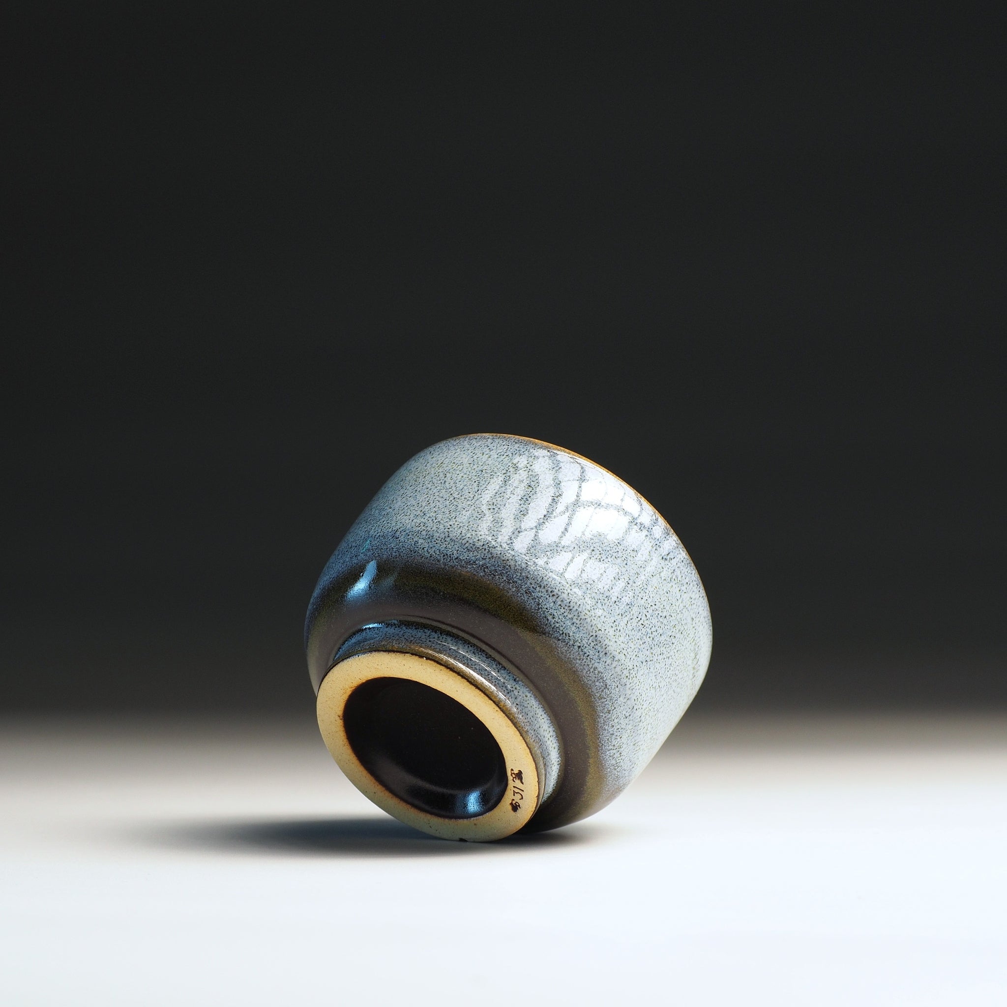 Side-bottom view of a Japanese pottery yunomi with azure textured surface on a gradient background