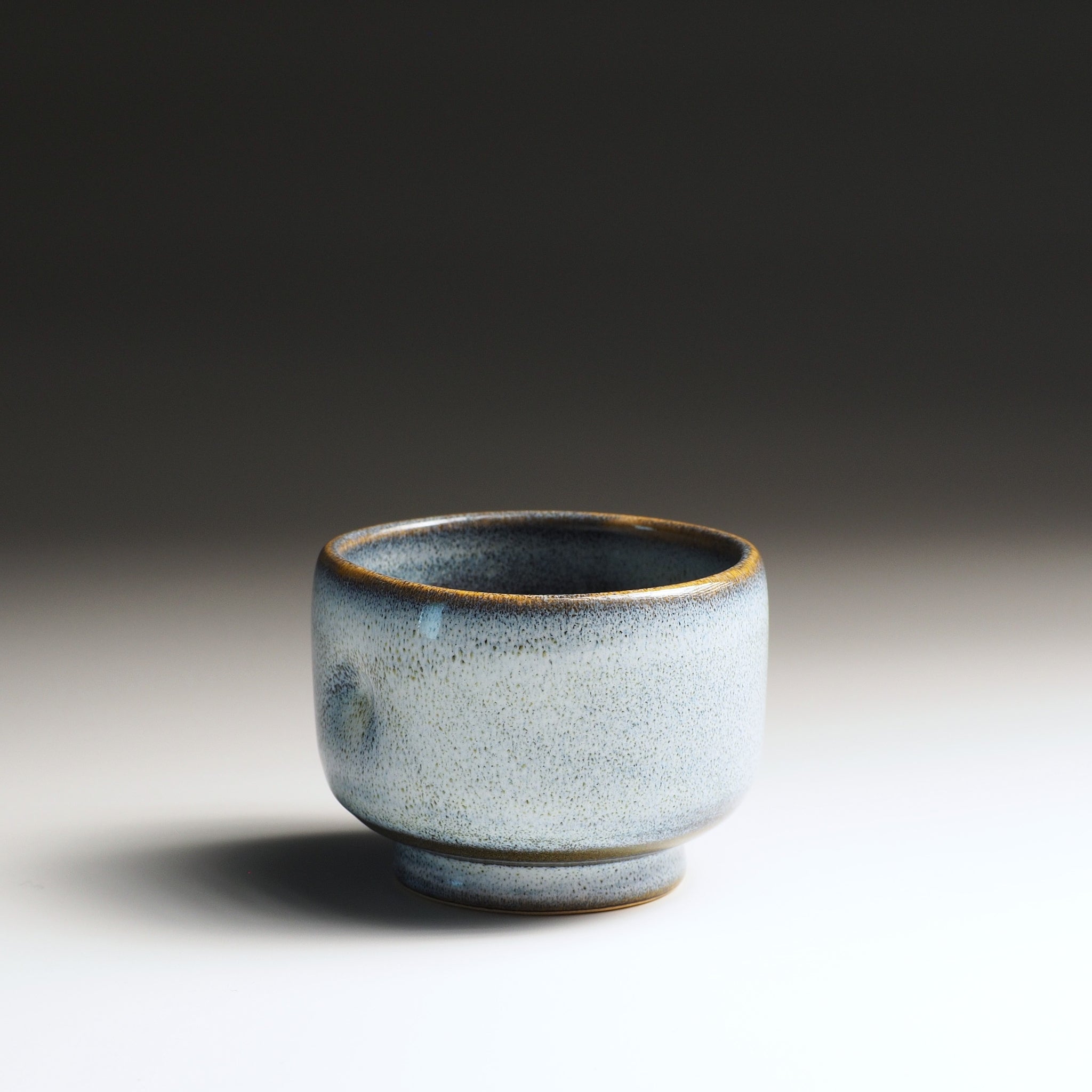 Light-blue pottery yunomi teacup on a studio gradient background