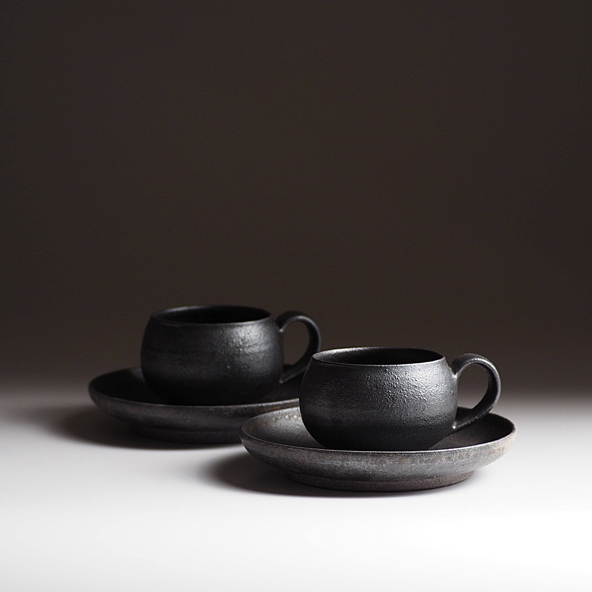 Two set of handcrafted black Japanese potteries espresso cup and saucer on gray background, Tsukush