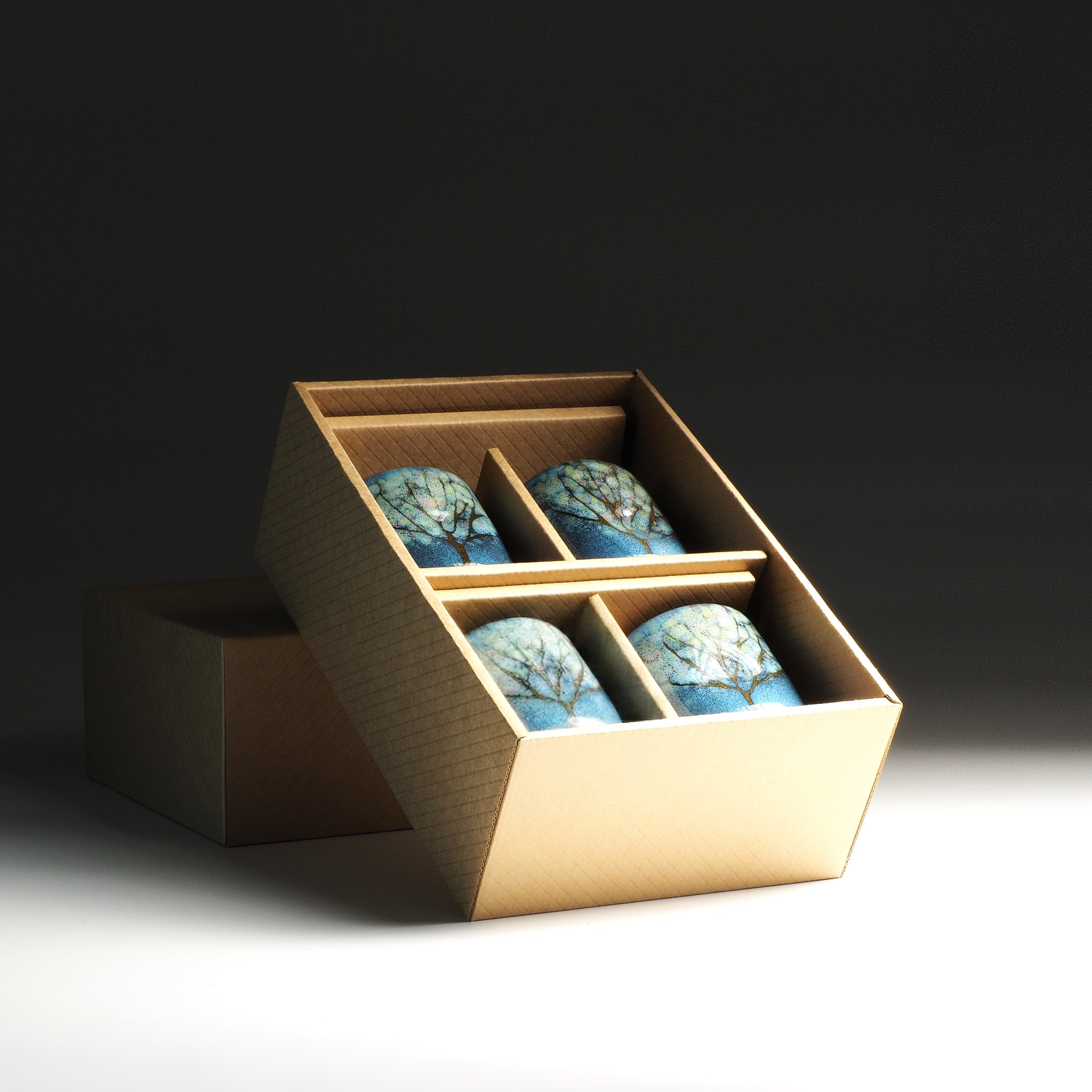 Open box with four blue Japanese yunomi on a dark background