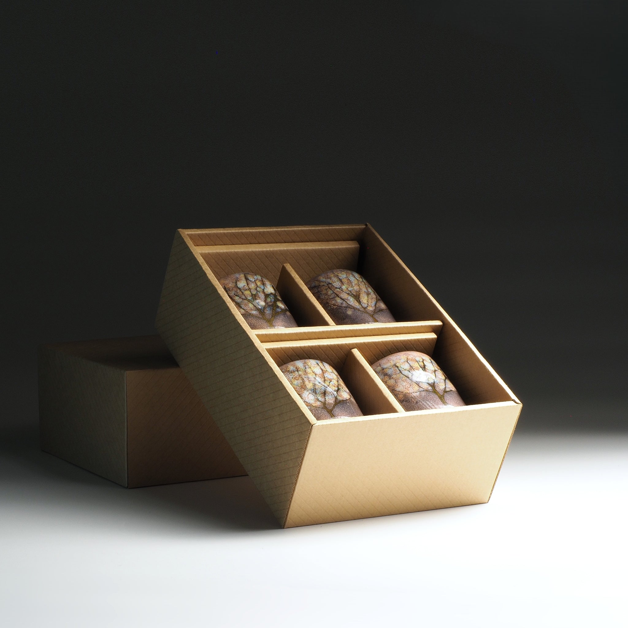 Open cardboard box with containing four japanese yunomi on a dark background