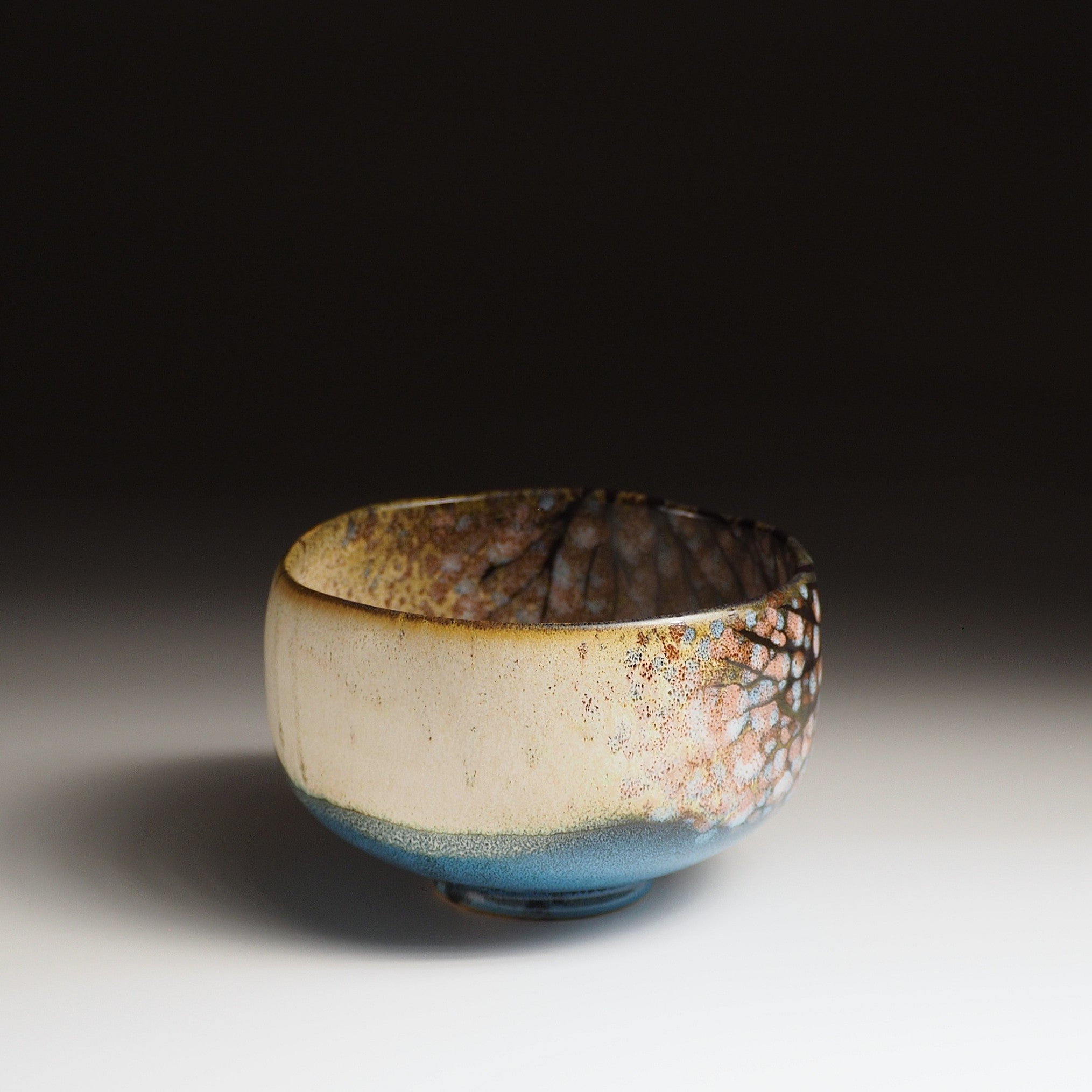 A Japanese ceramic matcha bowl, adorned with cherry blossoms and a tranquil lake, set against a black background. Tsukushi.