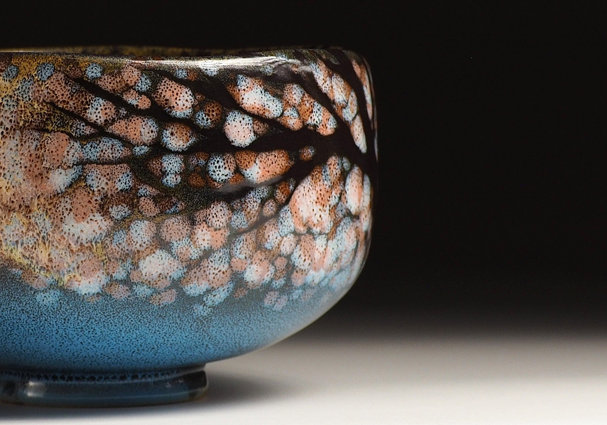A Close-up of Japanese ceramic matcha bowl adorned with cherry blossoms against a black background. Tsukushi