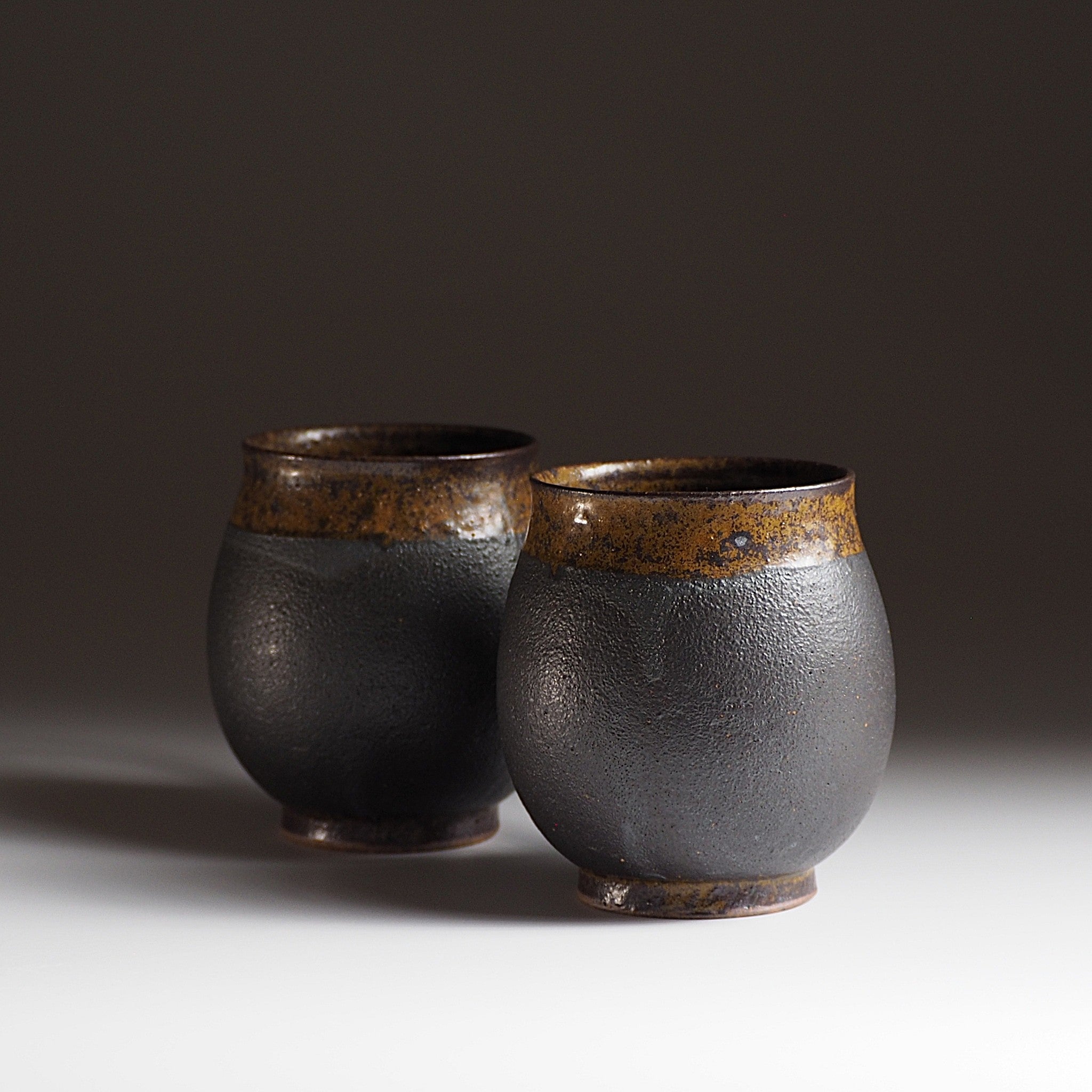 Handcrafted two black Japanese ceramic tea mugs on a beige gradation background, Tsukushi