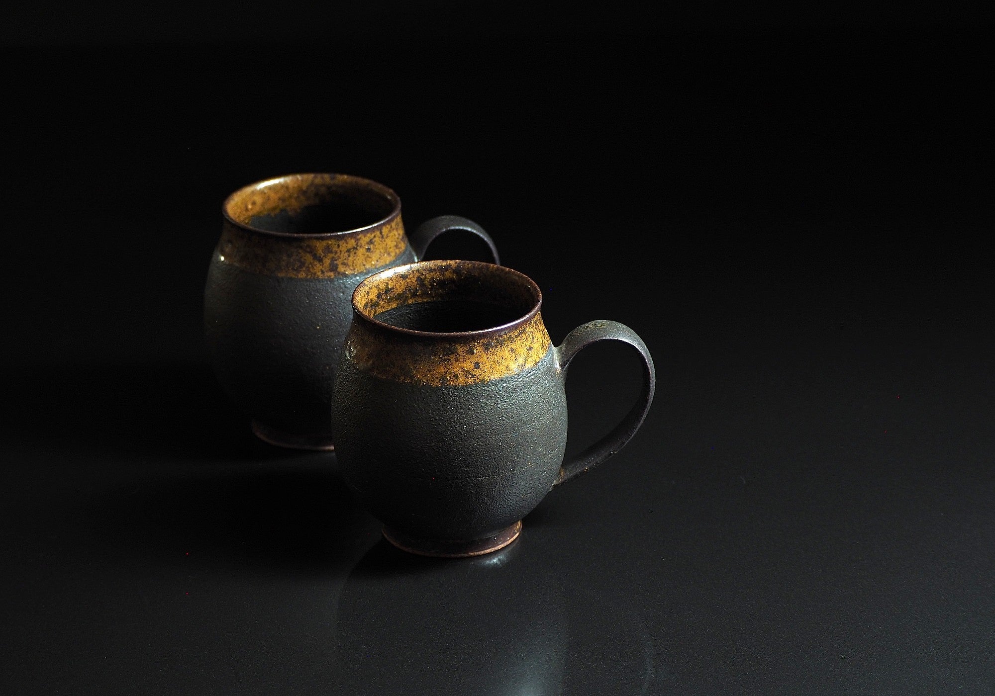 Handcrafted two  black Japanese ceramic tea mugs with a rustic finish on a black background, Tsukushi