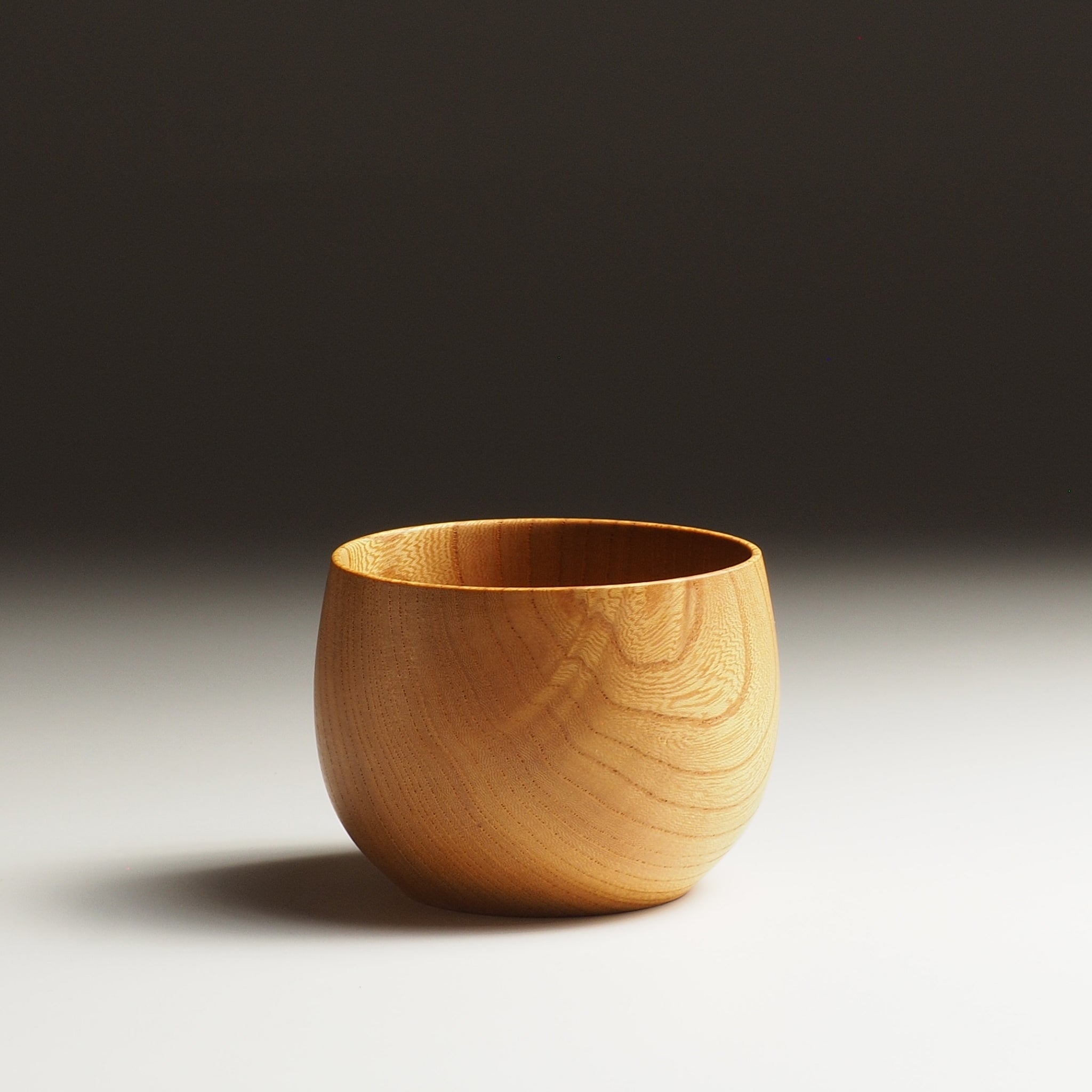 A side view of a Japanese wooden cup with a gradient background. Tsukushi