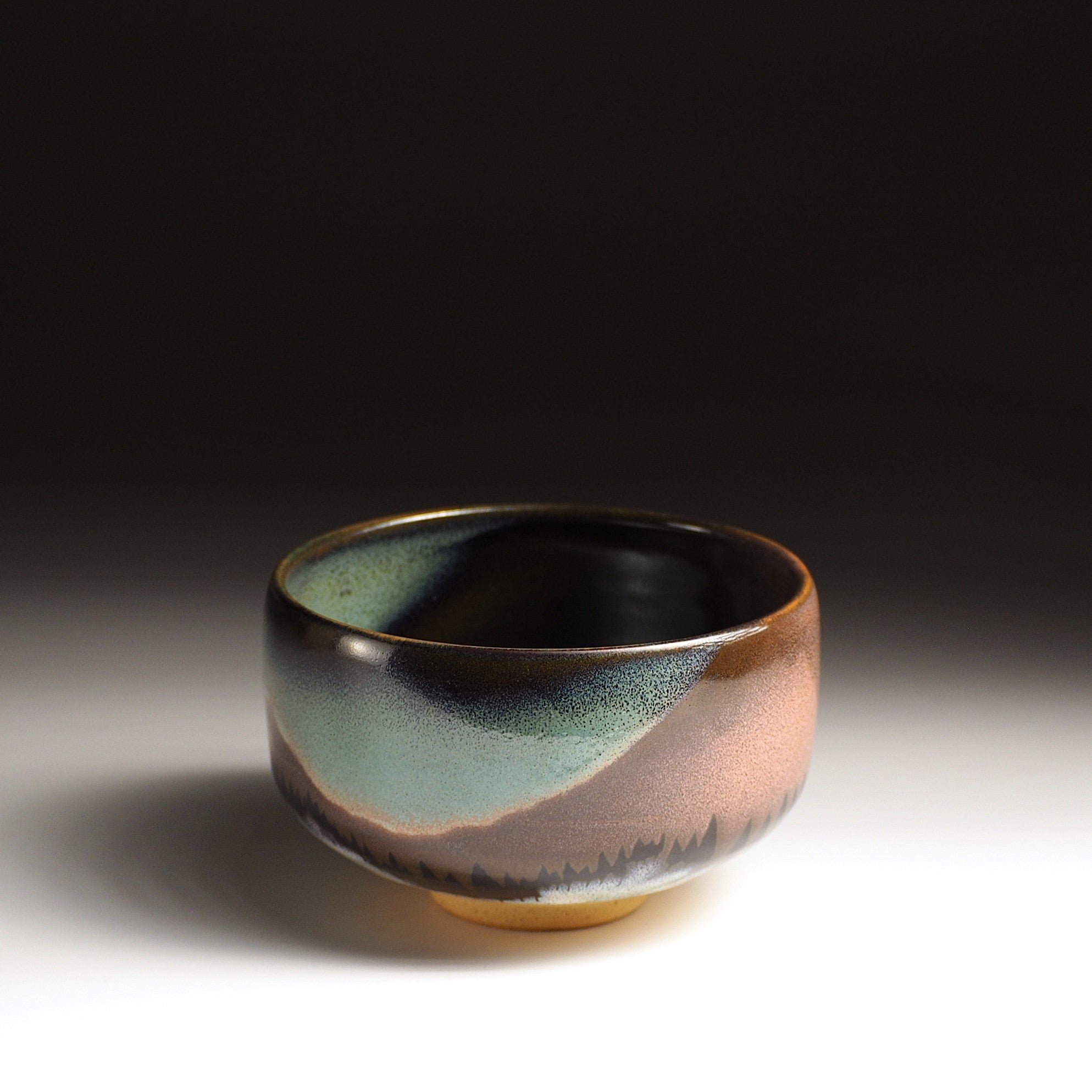 A Japanese ceramic matcha bowl adorned with an aurora and a mountain against a black background. Tsukushi