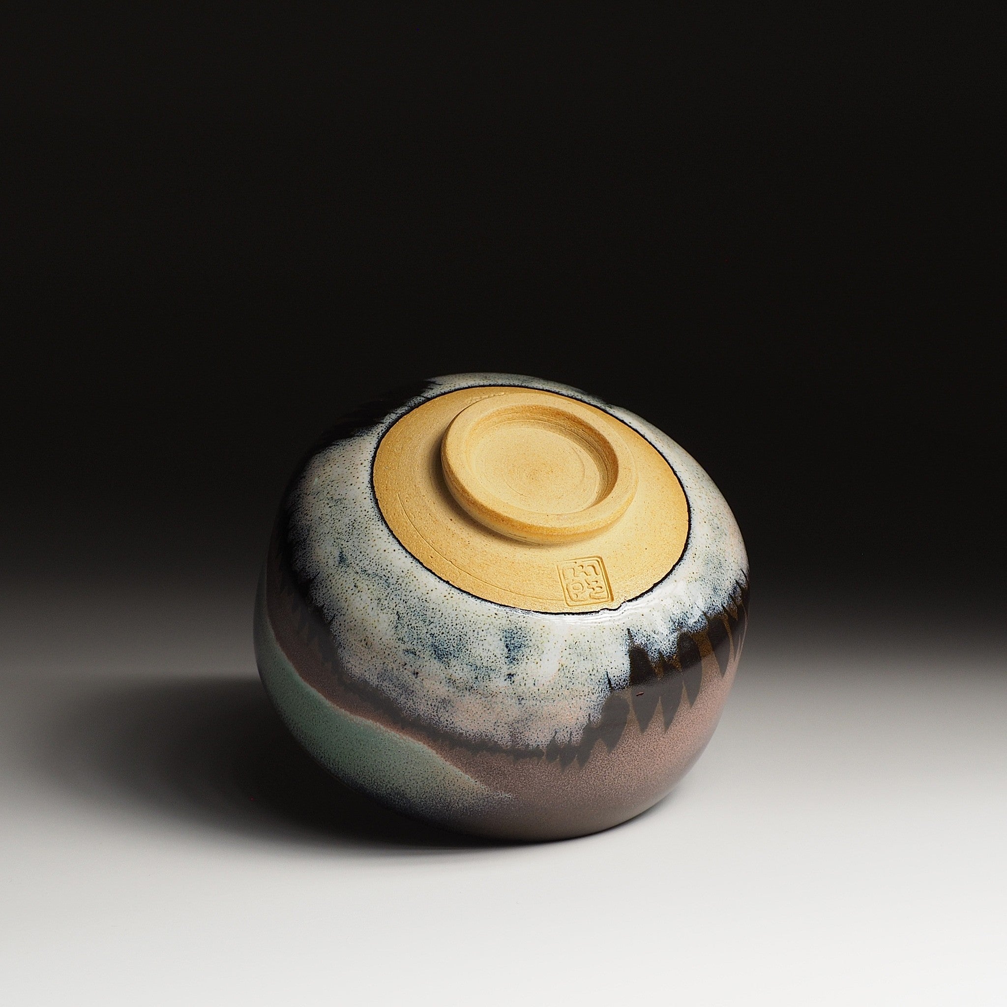 A bottom view of a Japanese ceramic matcha bowl adorned with a snow and a grove of tree against a black background. Tsukushi