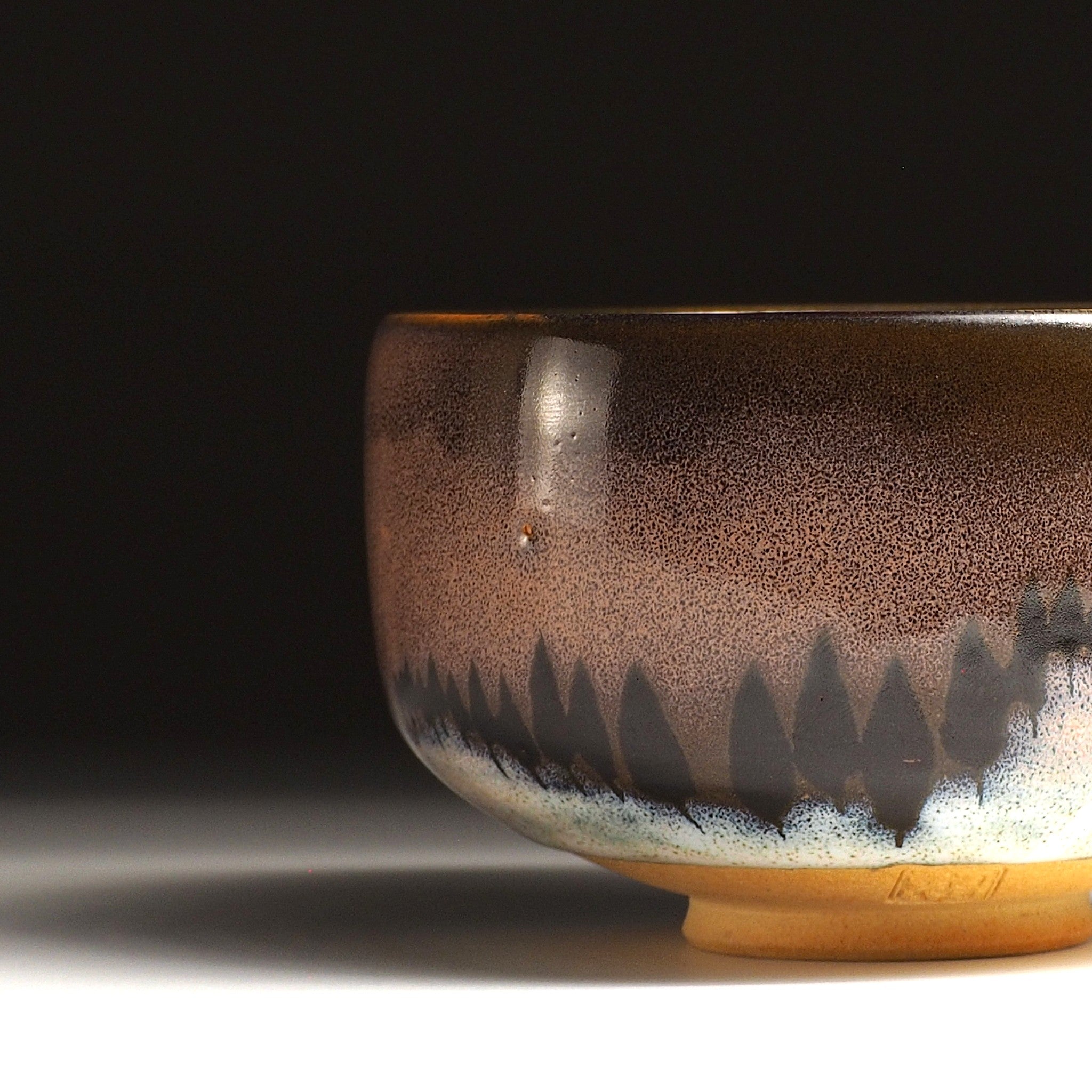 A Japanese ceramic matcha bowl adorned with an aurora and a grove of trees, set against a black background. Tsukushi