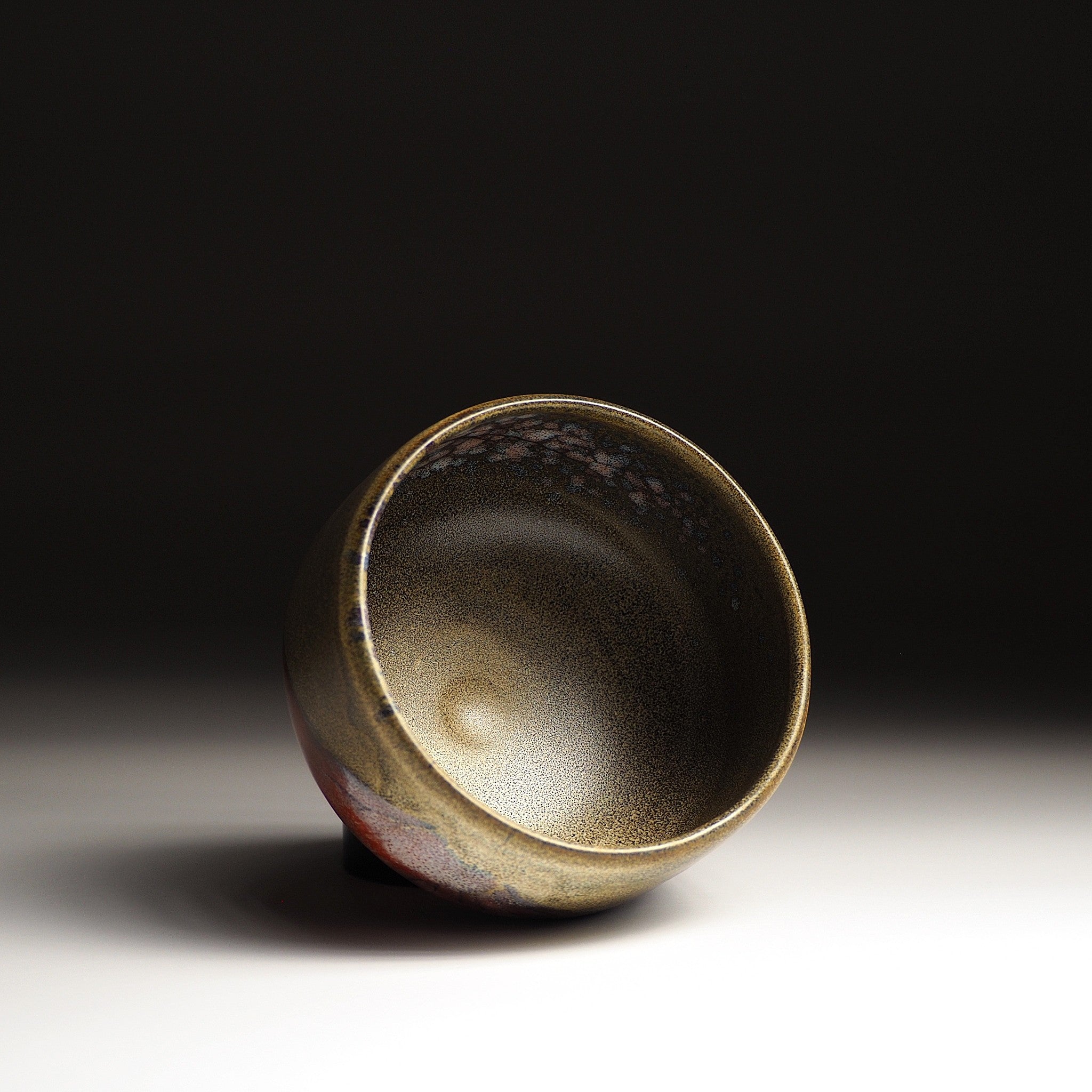 A top view of a Japanese ceramic matcha bowl adorned with Red Fuji on a brown surface, set against a black background. Tsukushi.
