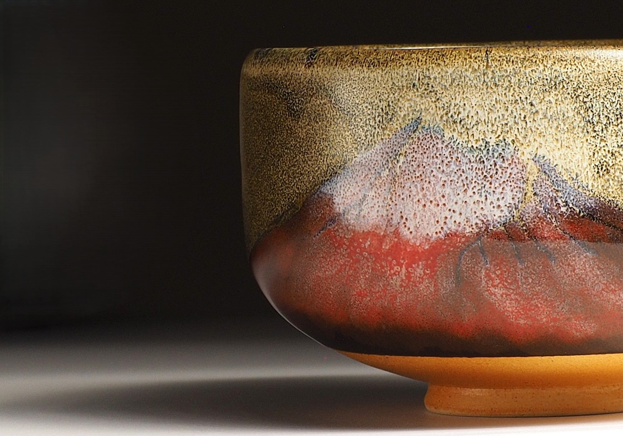 A close-up of a Japanese ceramic matcha bowl adorned with Mt.Red Fuji against a black background. Tsukushi