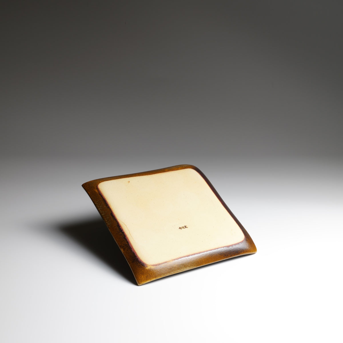 Underside of the handmade Akafuji square ceramic plate, showing its unglazed cream-colored base, maker's mark, and raised edges.