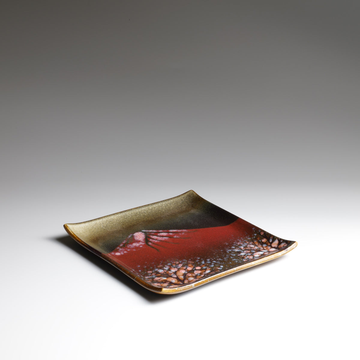 Angled view of the Akafuji square ceramic plate highlighting its gently curved shape, raised corners, and red Mount Fuji design.
