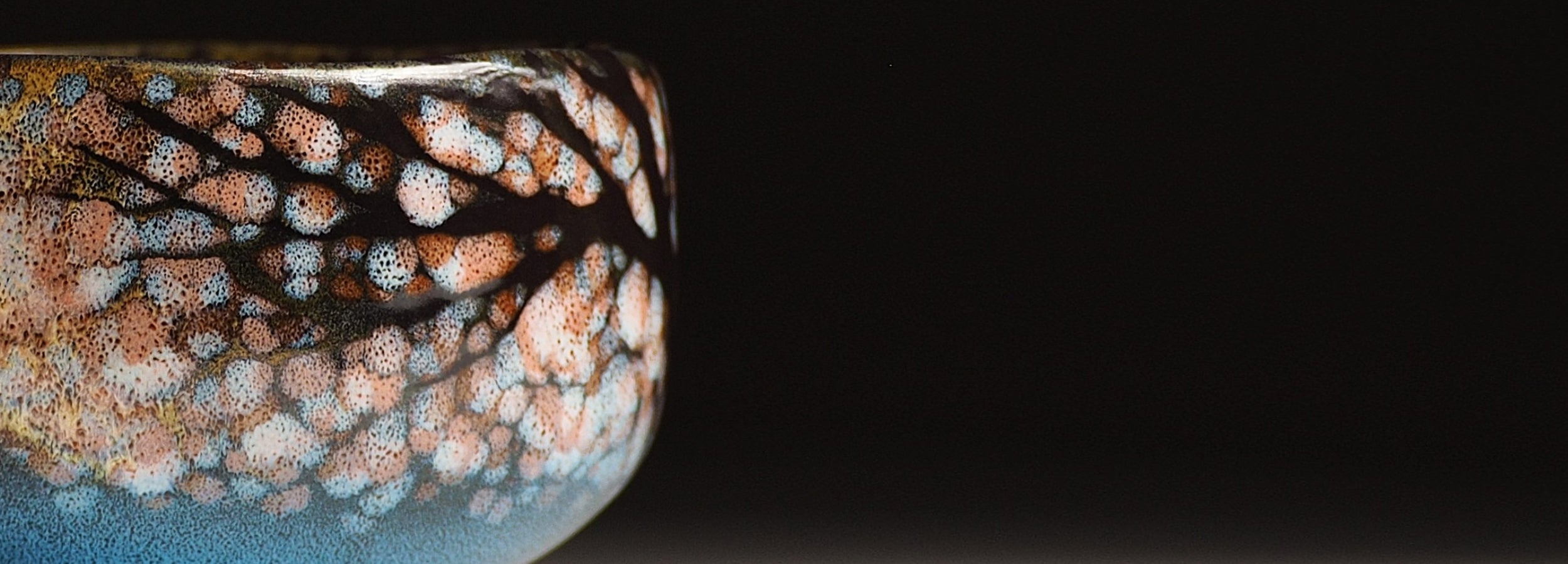 Close-up of a ceramic matcha bowl with textured surface on a black background. Tsukushi