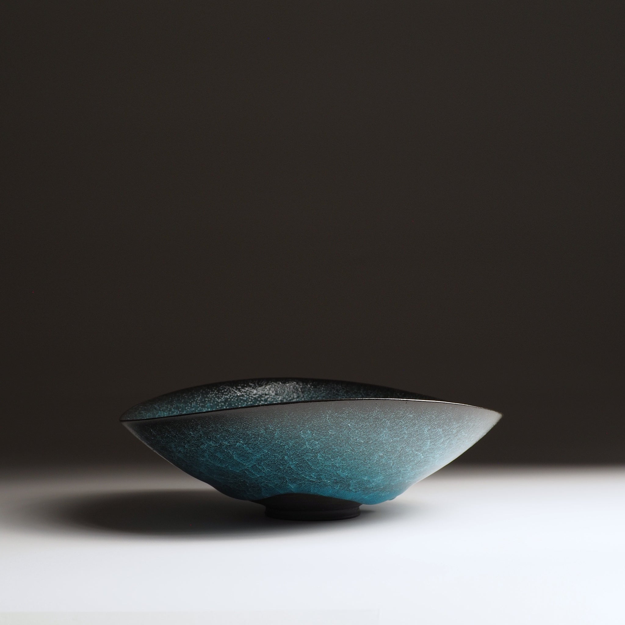 Aonami waved serving bowl, low angle view showing tapered rim and teal kannyu glaze gradient. Taichi Kawai, Usurai Pottery, Japan.