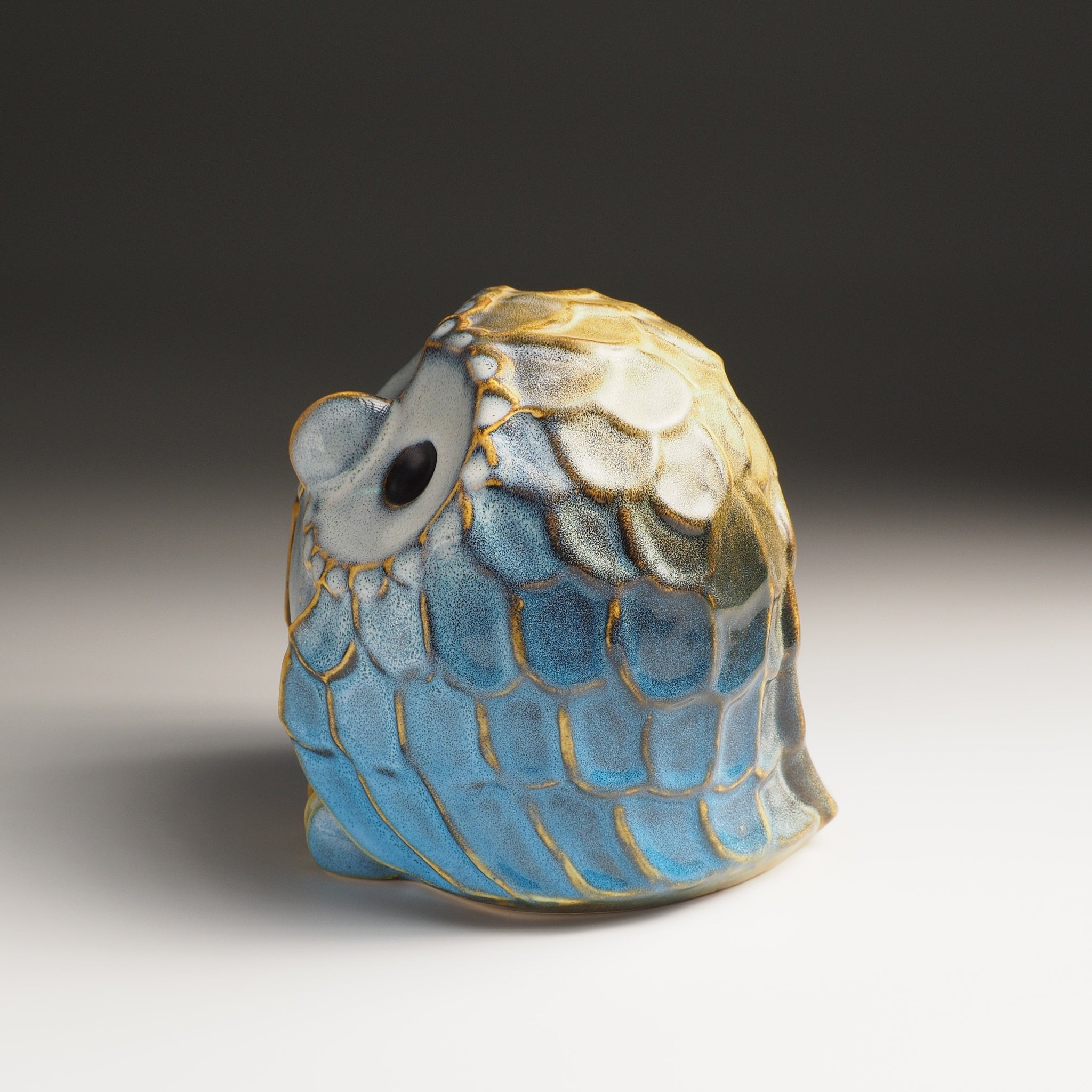 Left side view of the large Fukumori ceramic owl figurine, cerulean blue and gold Nanasai Tenmoku glaze.