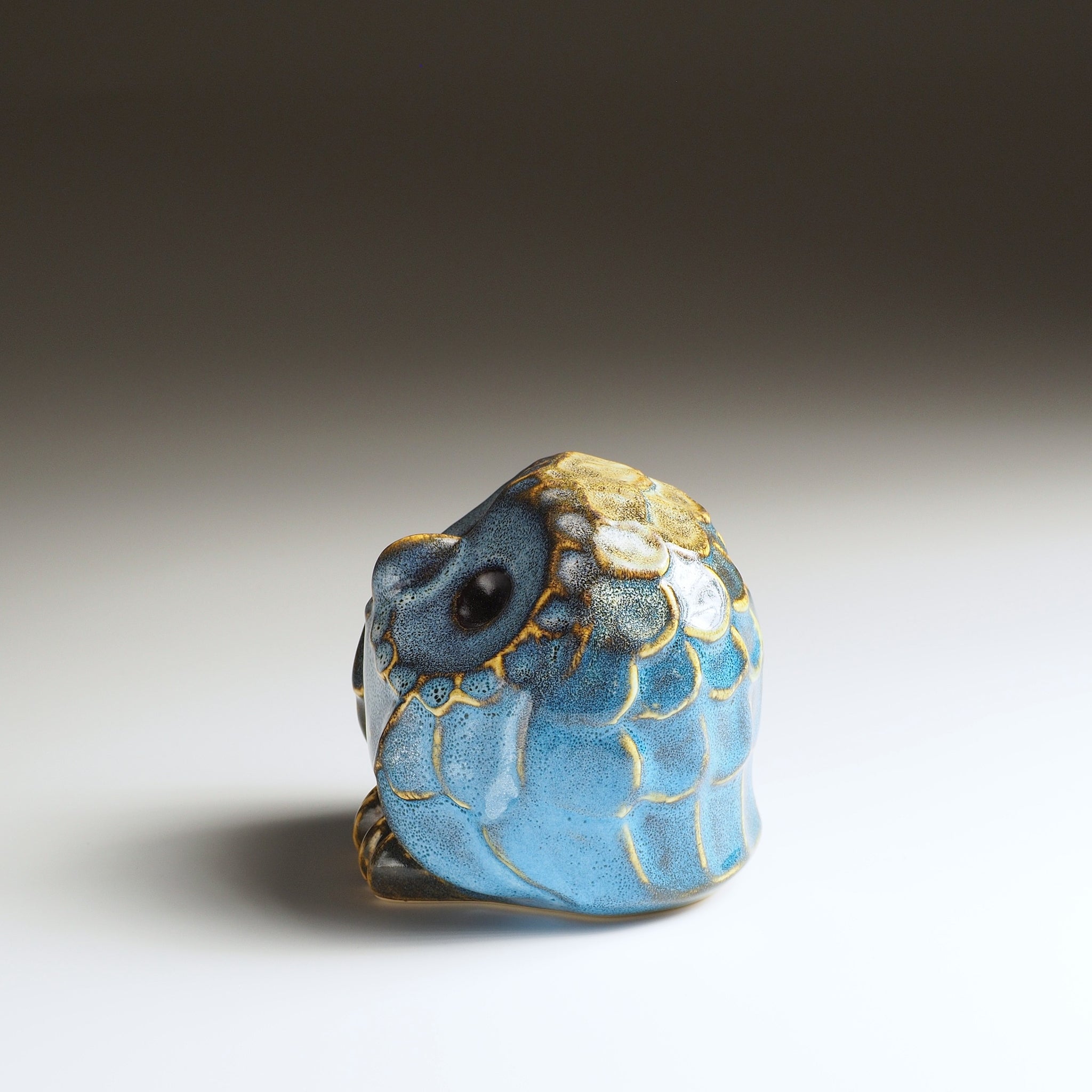 Side view of the small Fukumori ceramic owl ornament showing its rounded shape and layered feather decoration