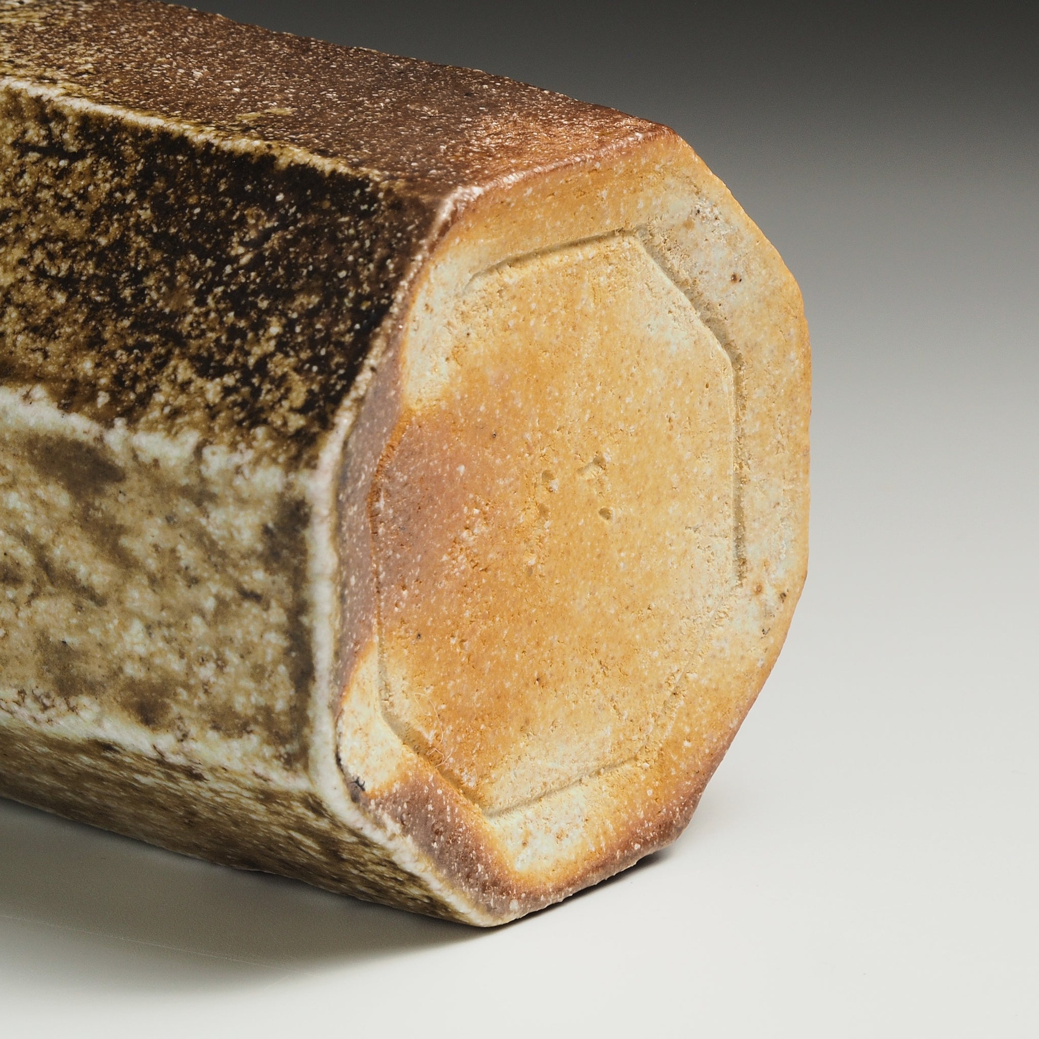 Close-up of a Hachiryō handmade Shigaraki cup showing its pale octagonal base and naturally varied brown surface.