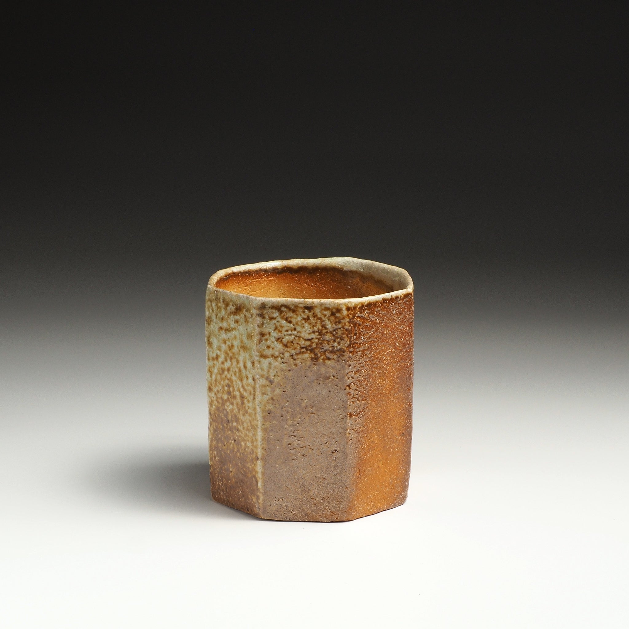 Angled view of a Hachiryō handmade Shigaraki cup showing its octagonal rim and warm earthy surface.