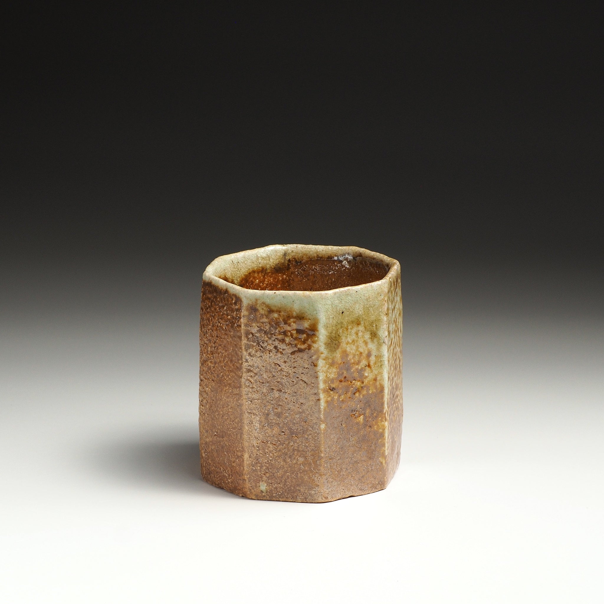 Angled view of a Hachiryō Shigaraki cup with a faceted body and naturally varied brown and beige tones.