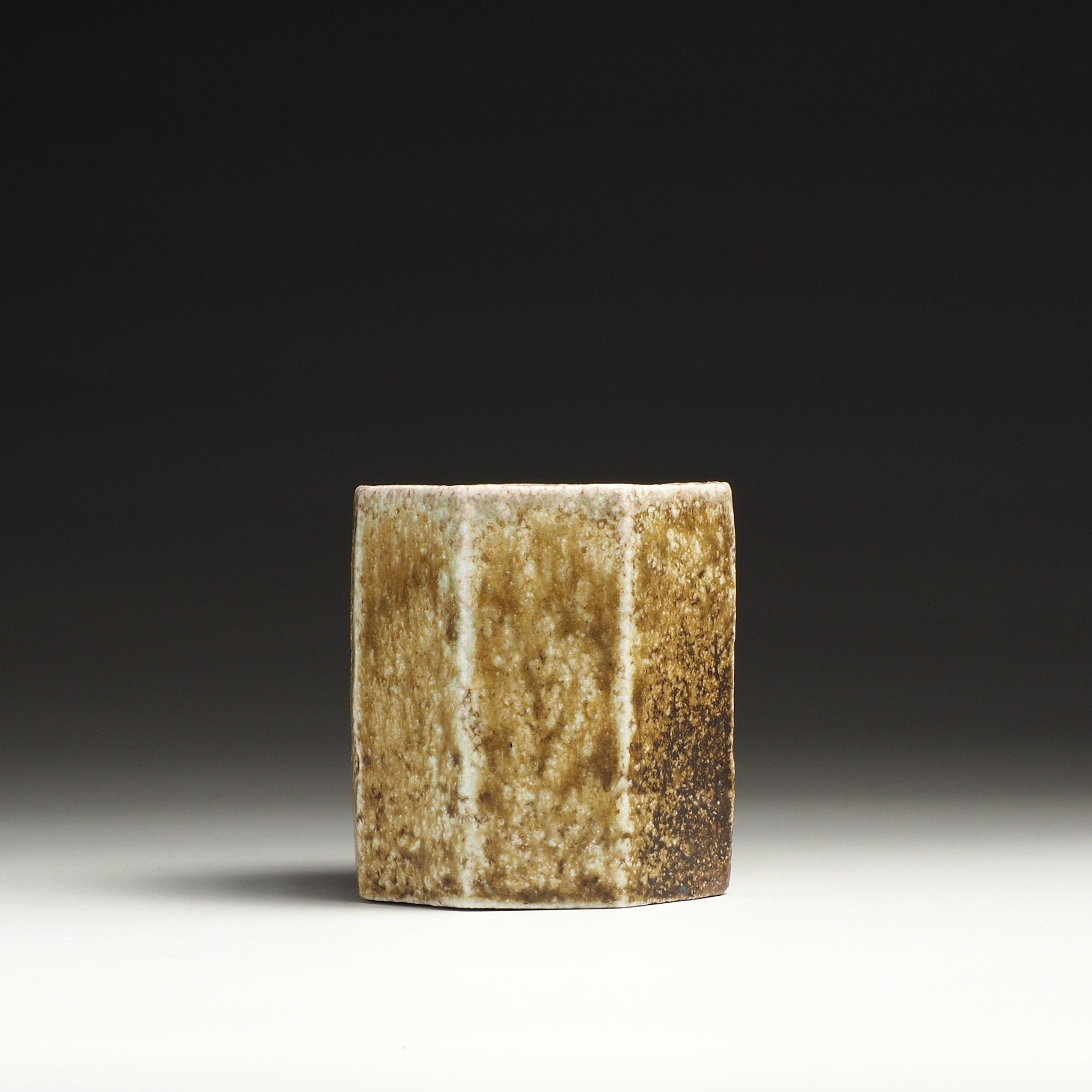 Side view of a Hachiryō Shigaraki cup with vertical beige, brown, and amber firing patterns.