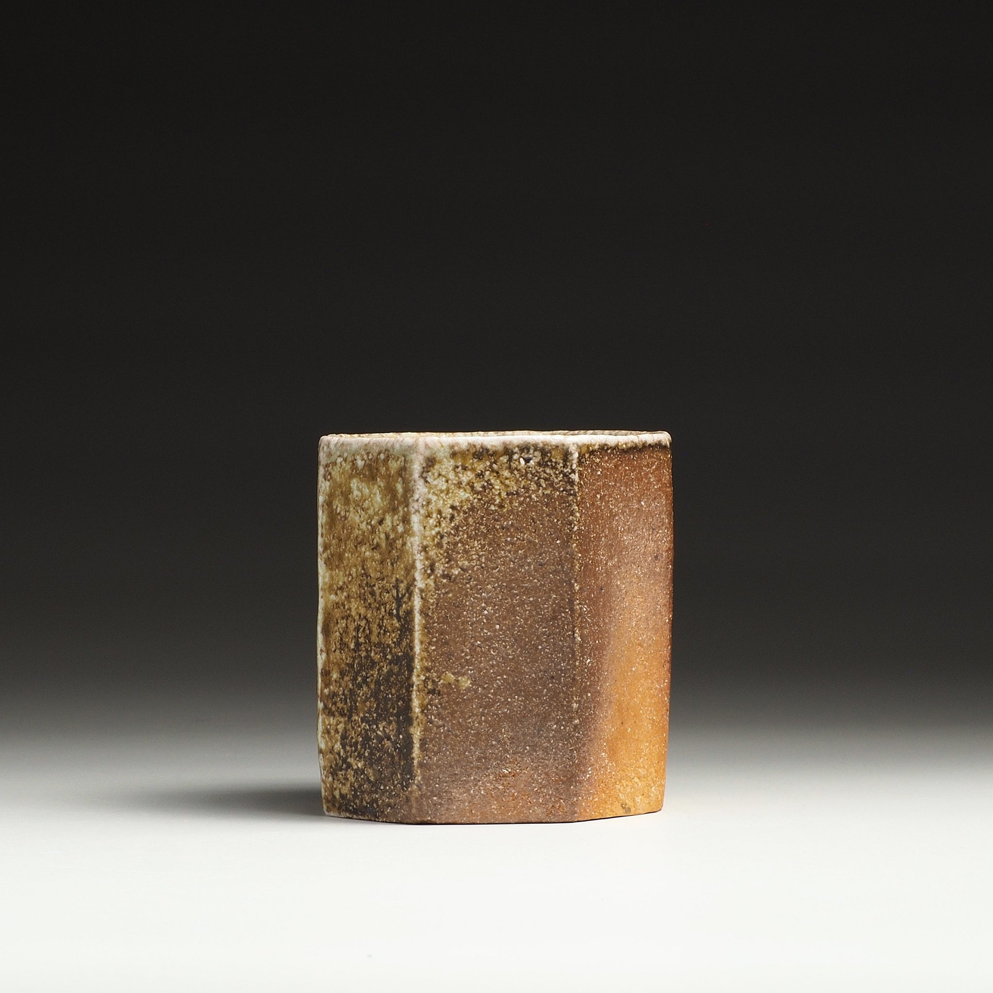 Side view of a Hachiryō handmade Shigaraki cup showing contrasting dark brown and warm amber surfaces.