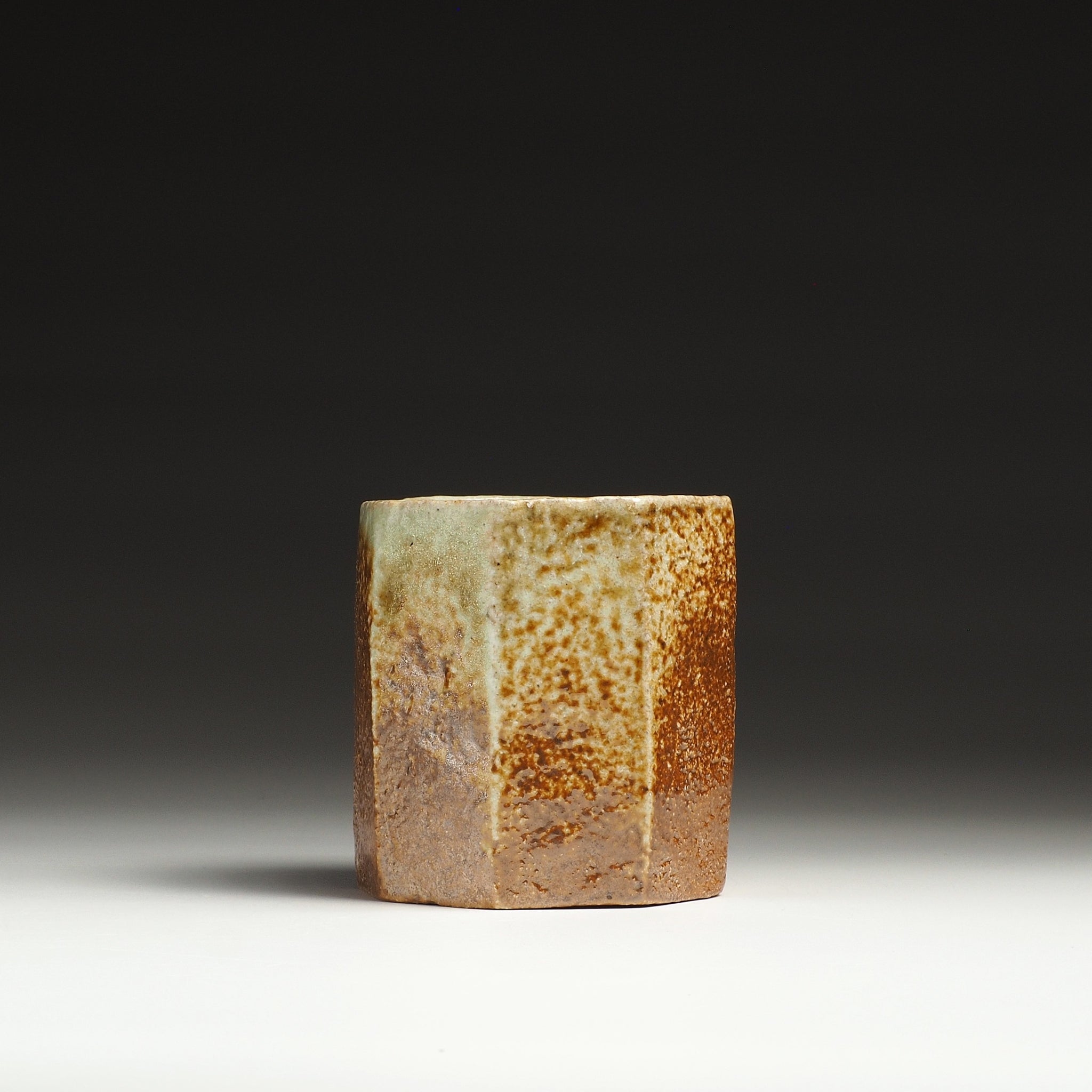 Side view of a Hachiryō Shigaraki cup with a mottled beige, rust-brown, and gray ceramic surface.