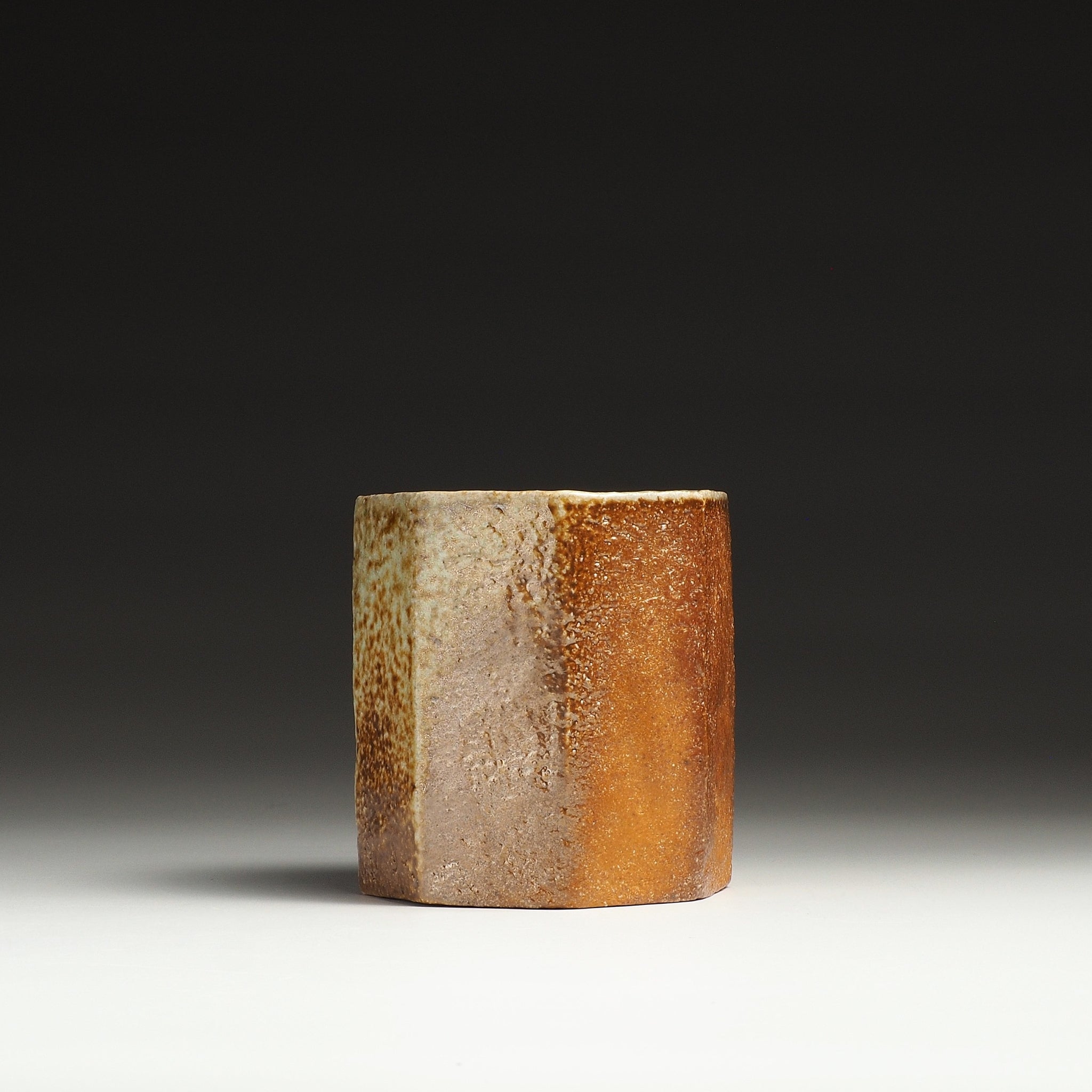 Hachiryō handmade Shigaraki cup showing contrasting pale beige and warm orange-brown faceted sides.