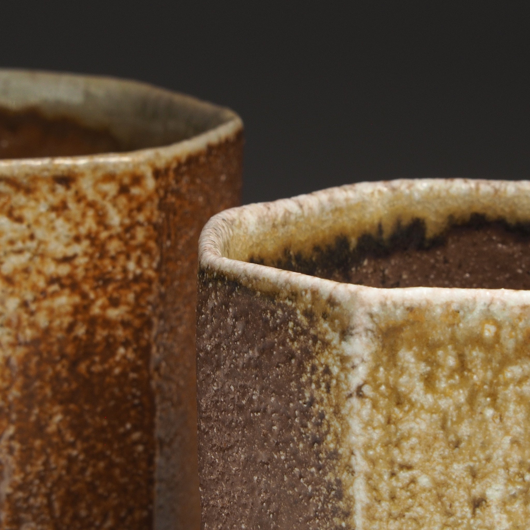 Close-up of two Hachiryō handmade Shigaraki cups showing their irregular octagonal rims and contrasting brown and beige glazed surfaces.