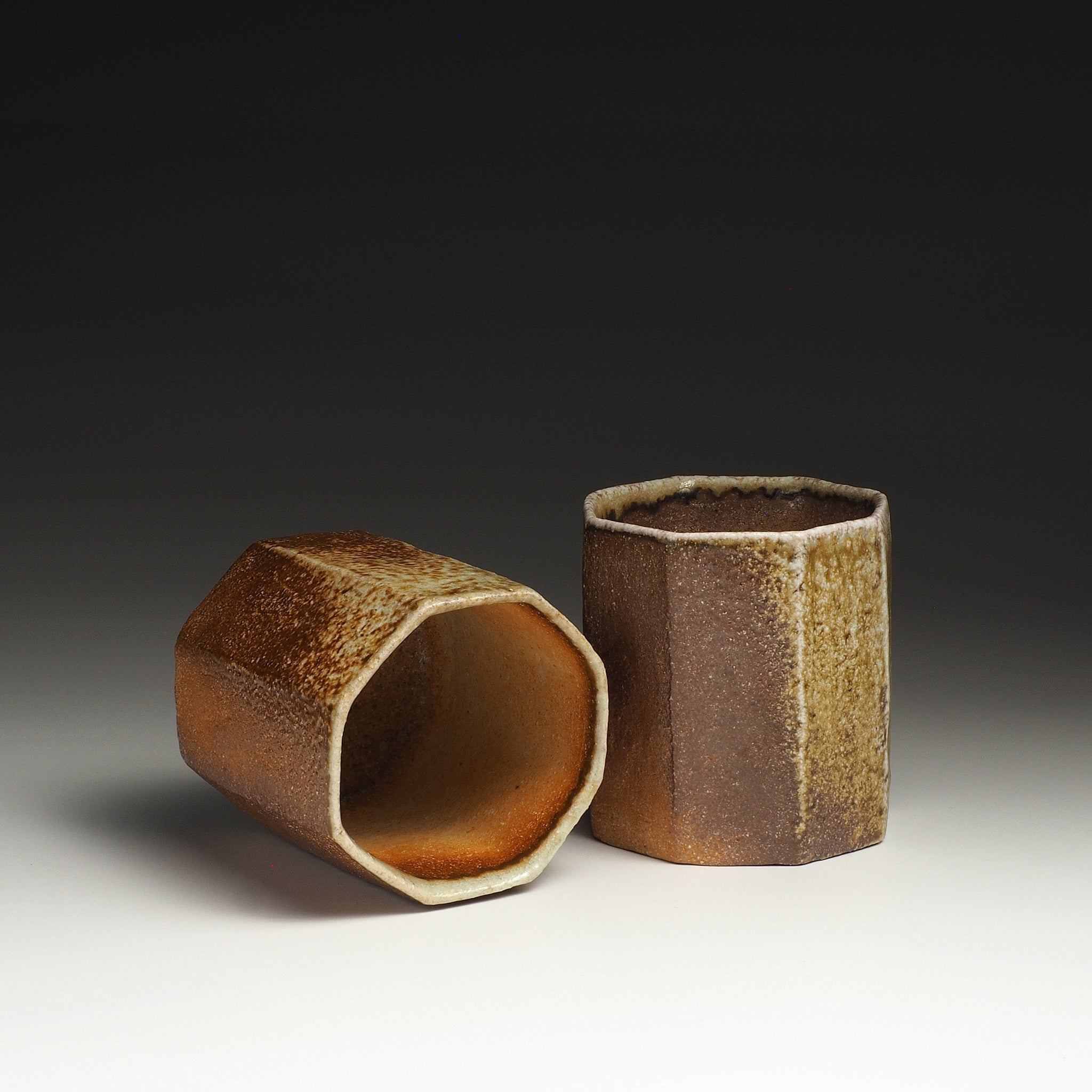 Two Hachiryō handmade Shigaraki cups with octagonal forms and naturally varied brown, beige, and amber surfaces.