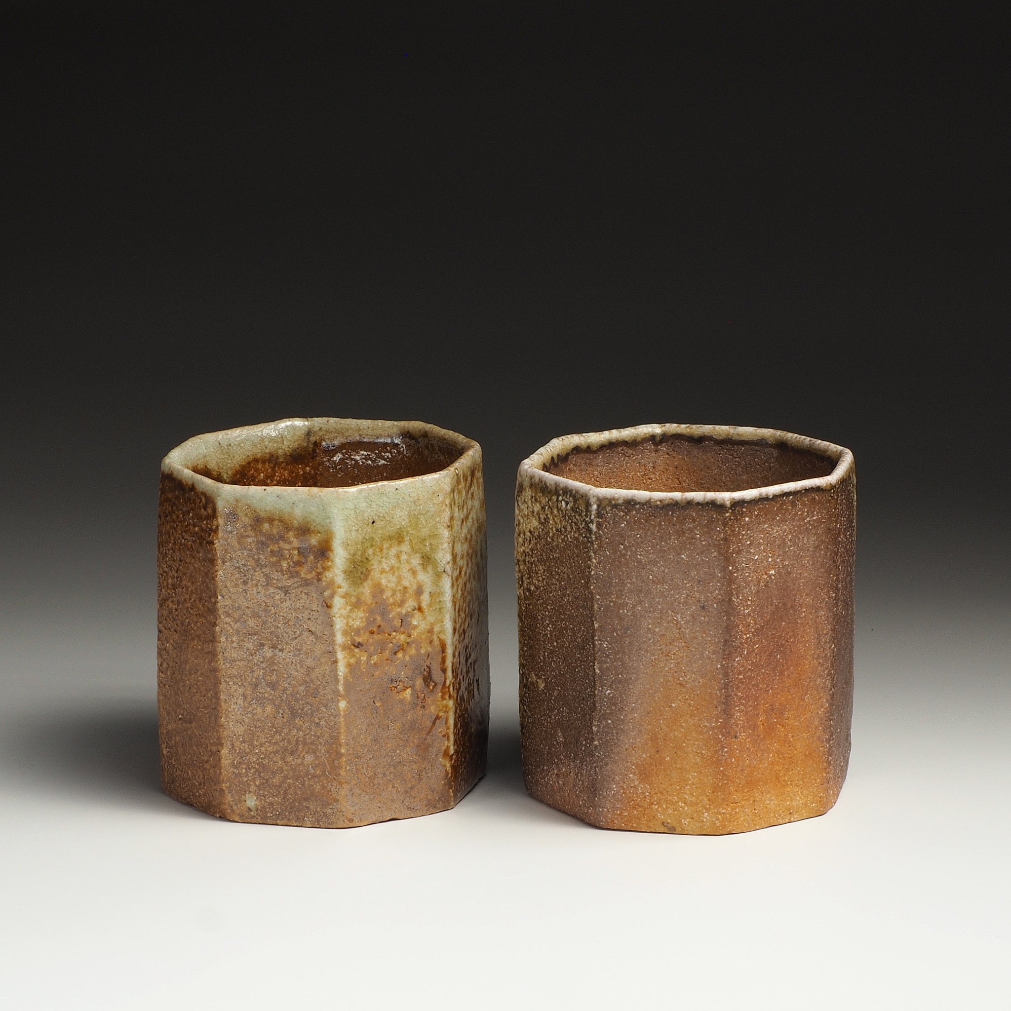 Two Hachiryō Shigaraki cups side by side with contrasting beige, brown, and amber natural firing tones.