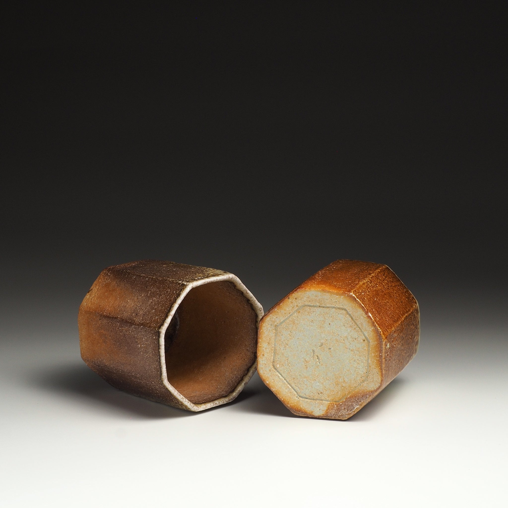 Two Hachiryō Shigaraki cups resting on their sides, showing an octagonal opening and pale ceramic base.