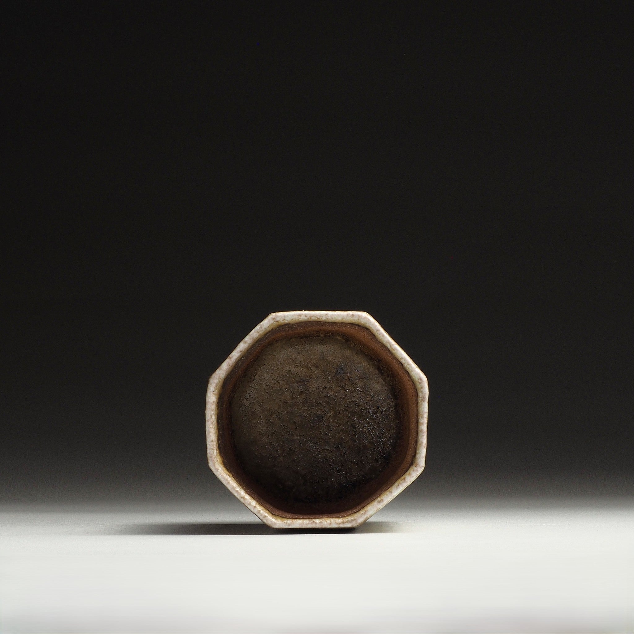 Interior view of a Hachiryō handmade Shigaraki cup showing its octagonal opening and dark brown inner surface.