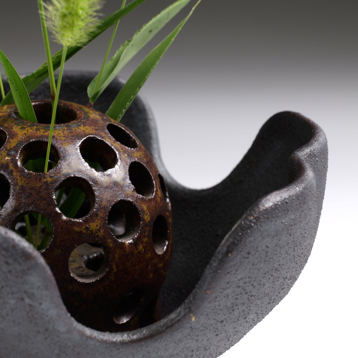 Detail view of the ceramic hanamori flower frog with foxtail grass on a faded background