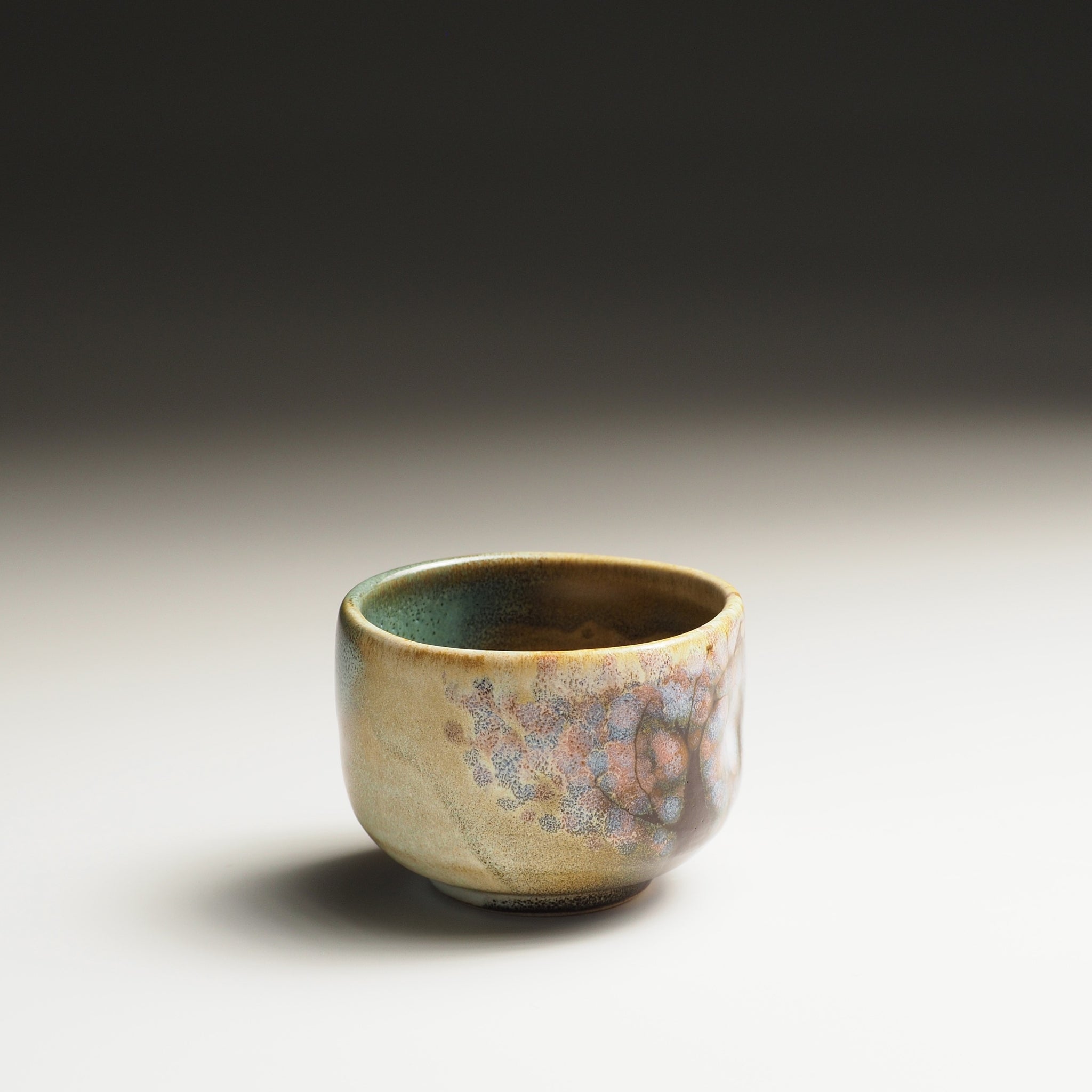 Guinomi sake cup with a textured surface and sakura decorations on a gradient background