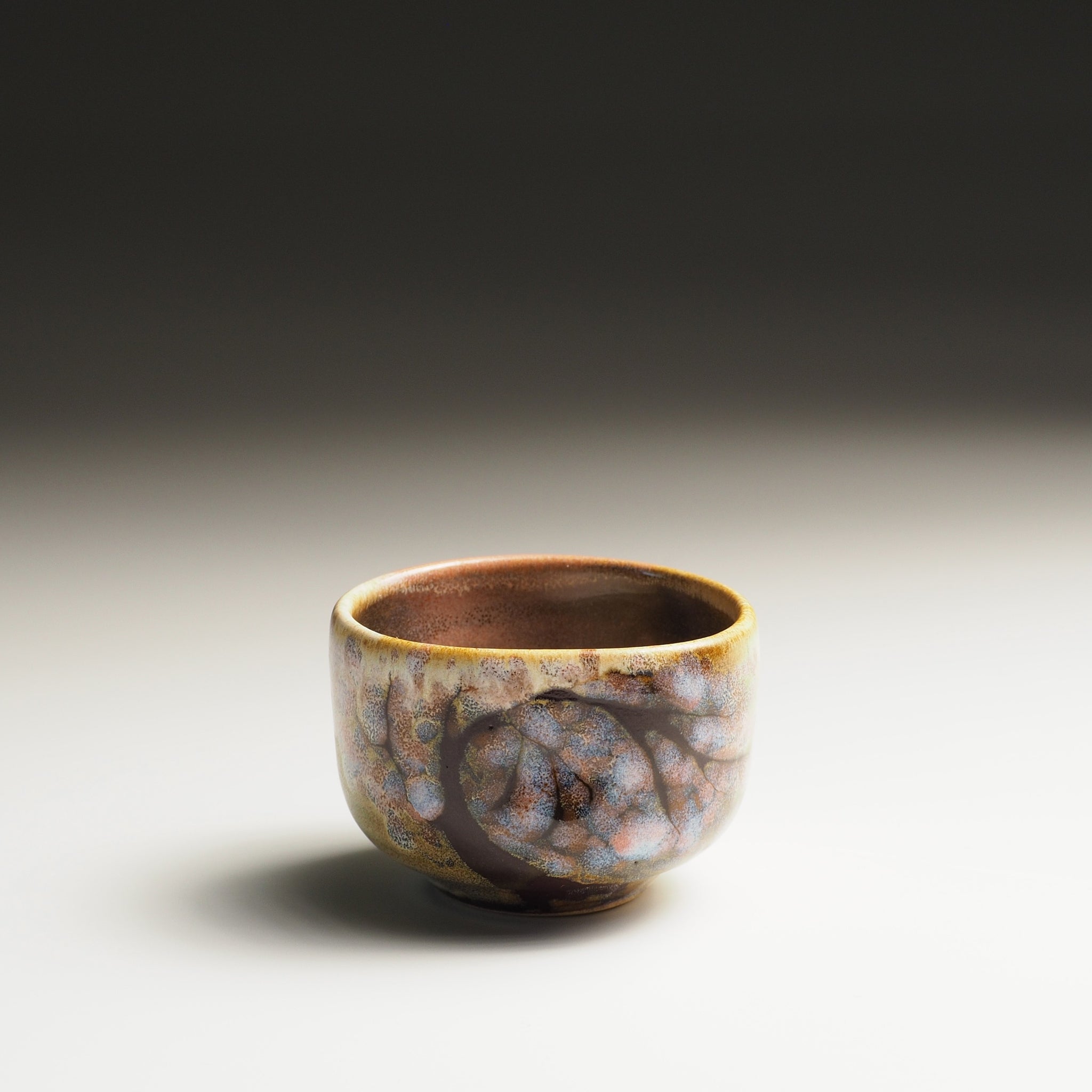 Japanese ceramic sake cup with a textured surface on a gradient background