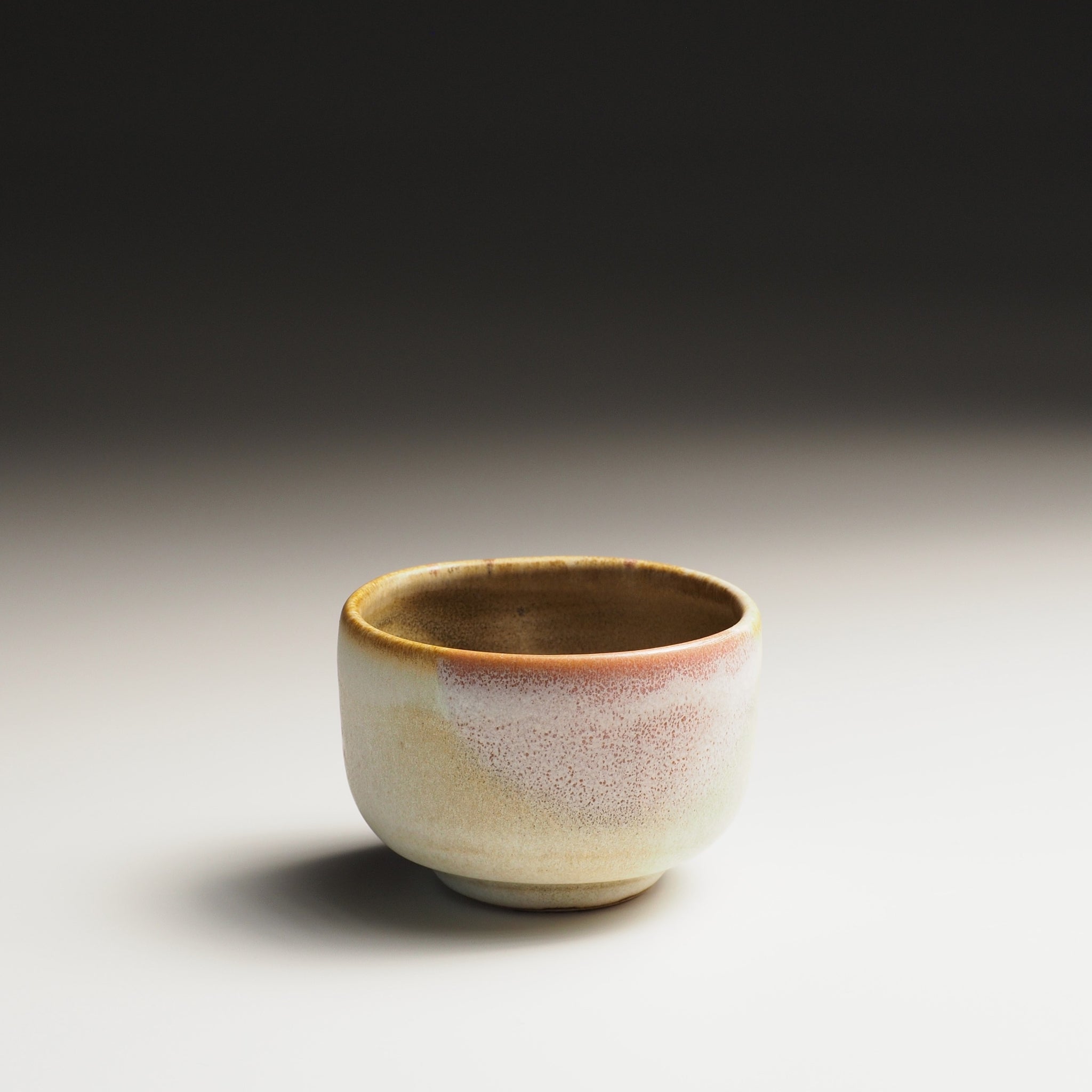 Front view of a Japanese sake cup with a textured surface and sakura decorations on a gradient background
