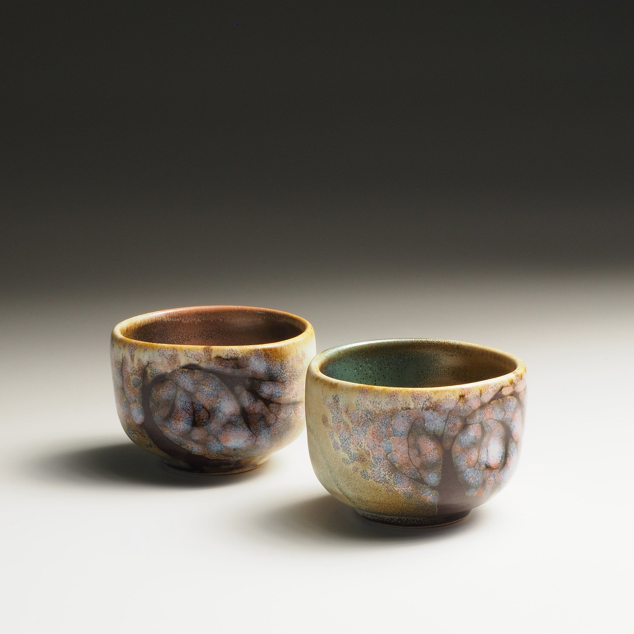 Two Japanese sake cups with a textured surface and sakura decorations