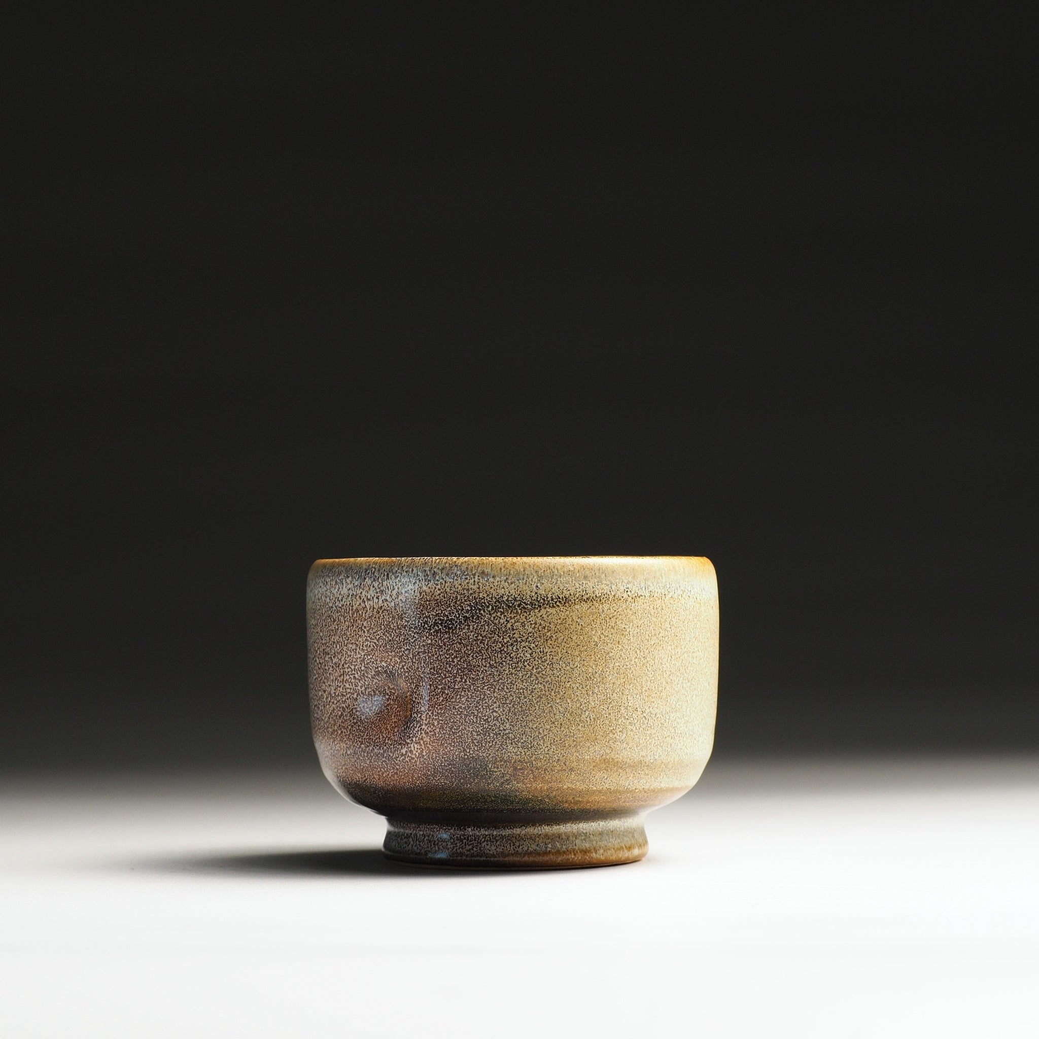 Front view of a small ceramic yunomi cup with a gradient finish on a dark background
