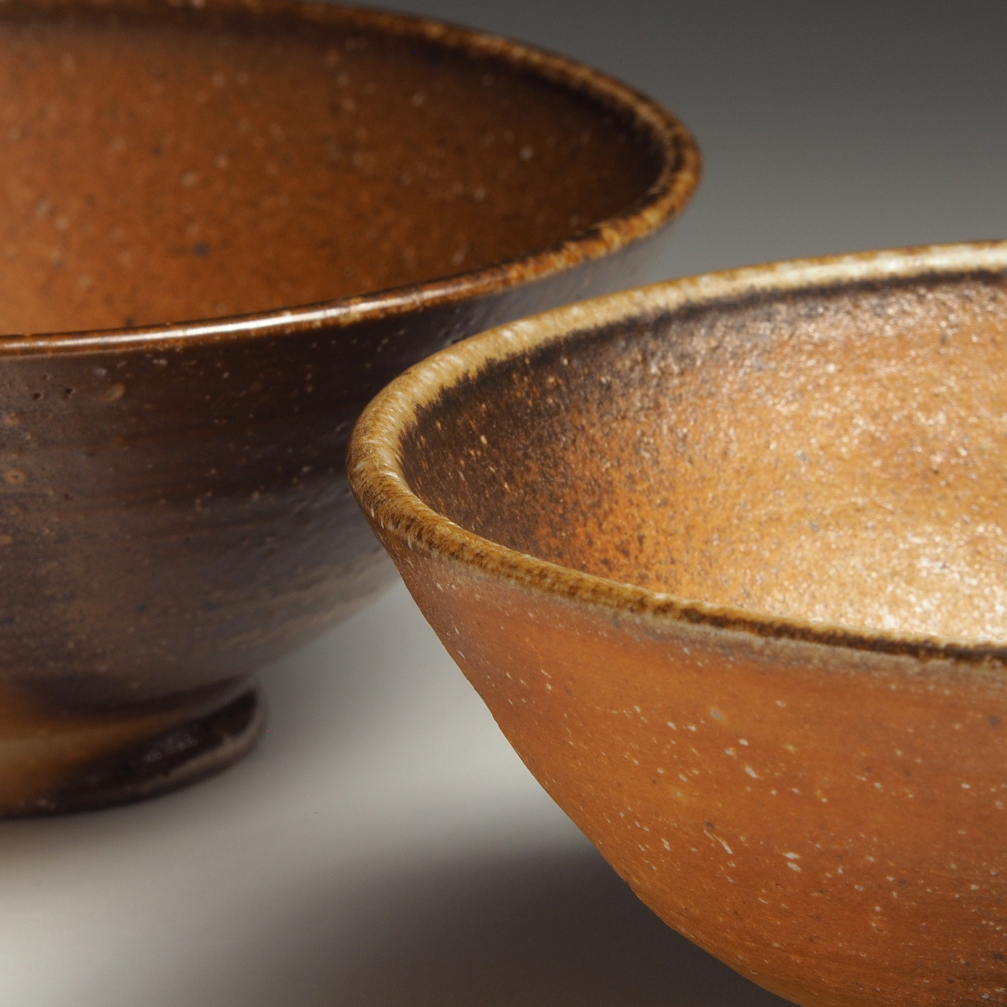 Close-up of two Mizuho handmade Shigaraki rice bowls showing contrasting dark brown and warm amber interiors with softly varied natural glaze.