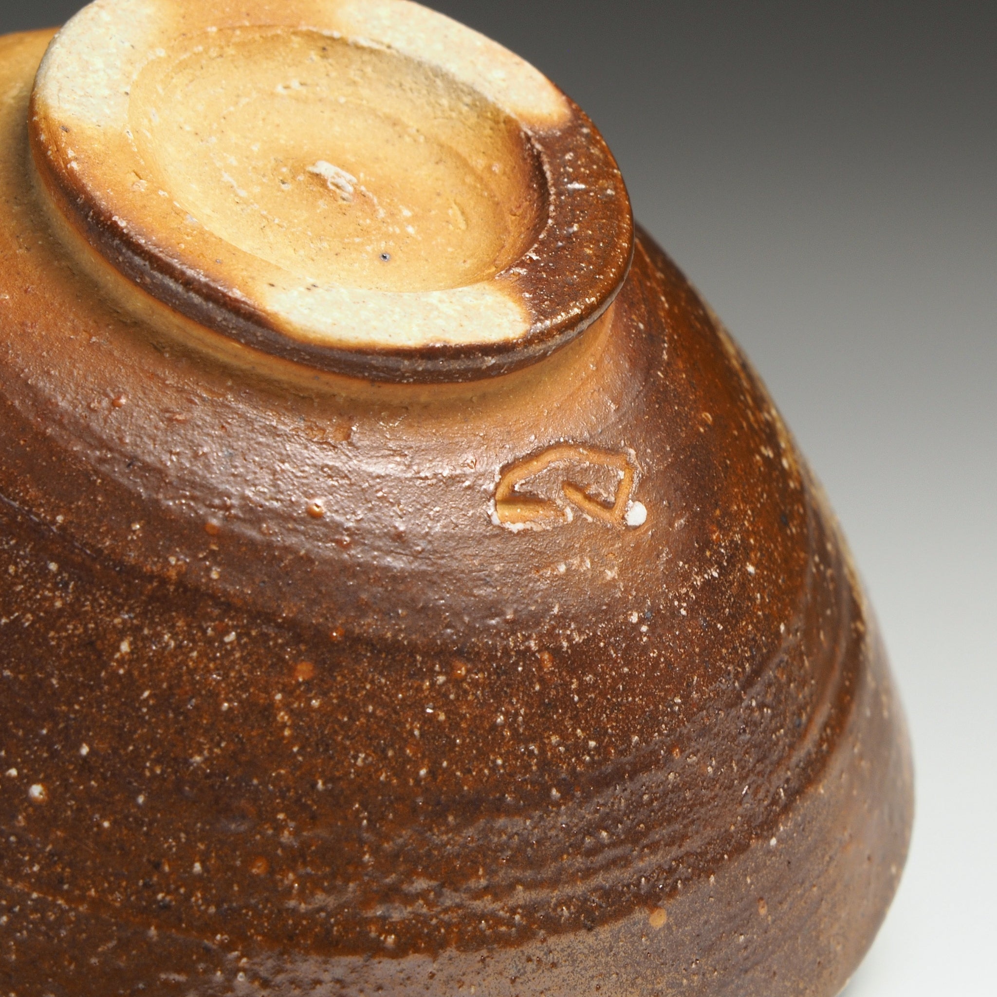 Close-up of the underside of a Mizuho handmade Shigaraki rice bowl showing the foot ring, dark brown fired surface, and impressed kiln mark.