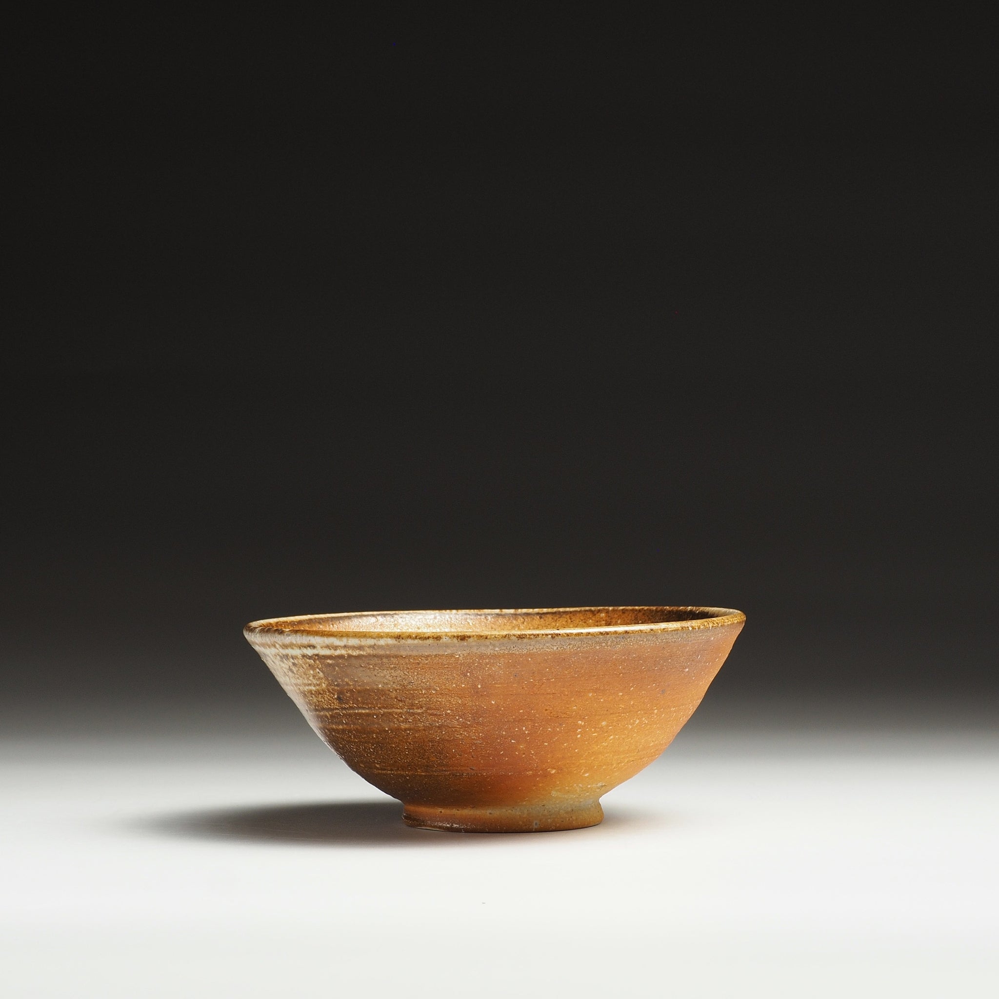 Side view of a Mizuho handmade Shigaraki rice bowl with a pale beige upper surface and warm brown base.