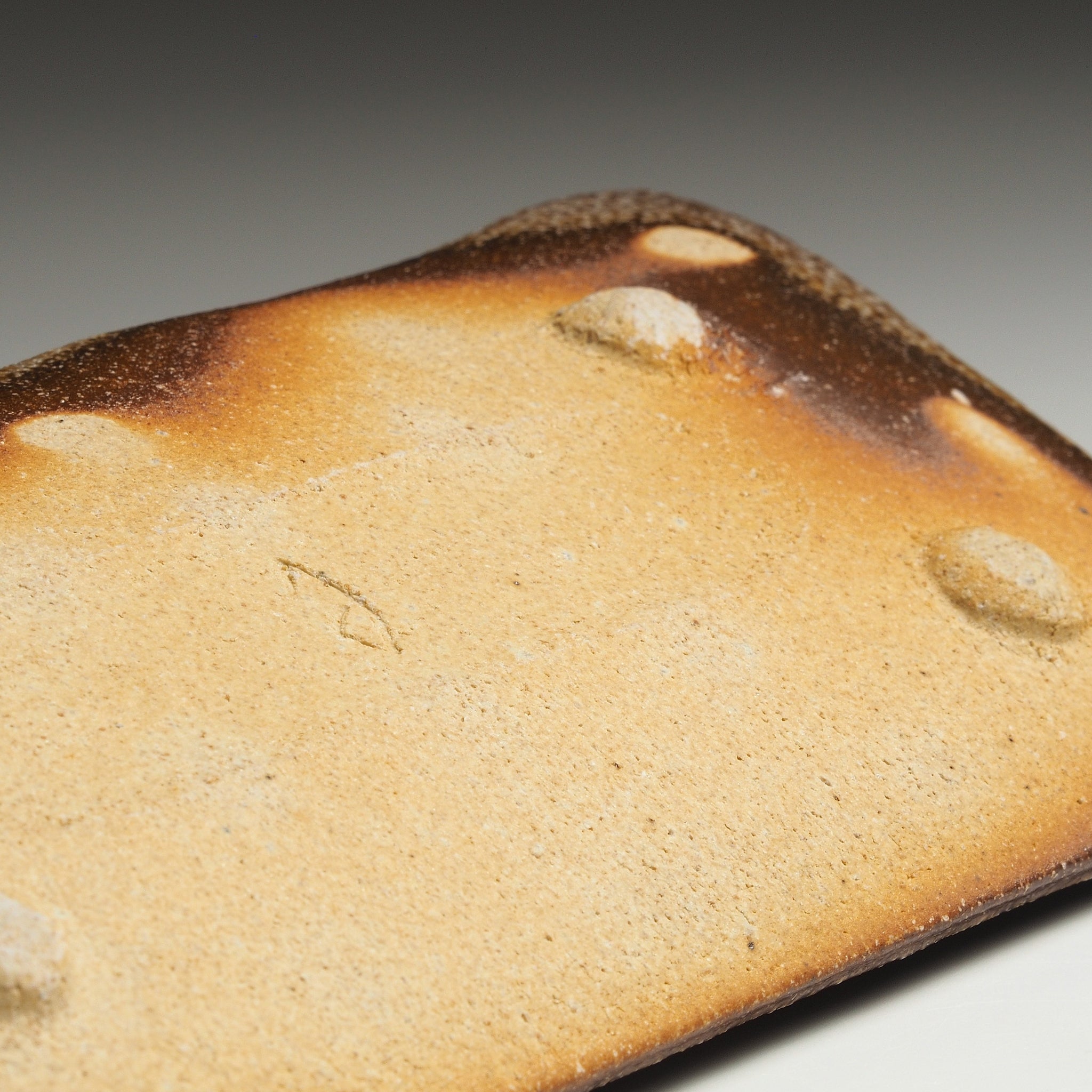 Close-up of the underside of the Nagafune handmade Shigaraki serving plate showing its pale base, raised feet, natural firing marks, and kiln mark.