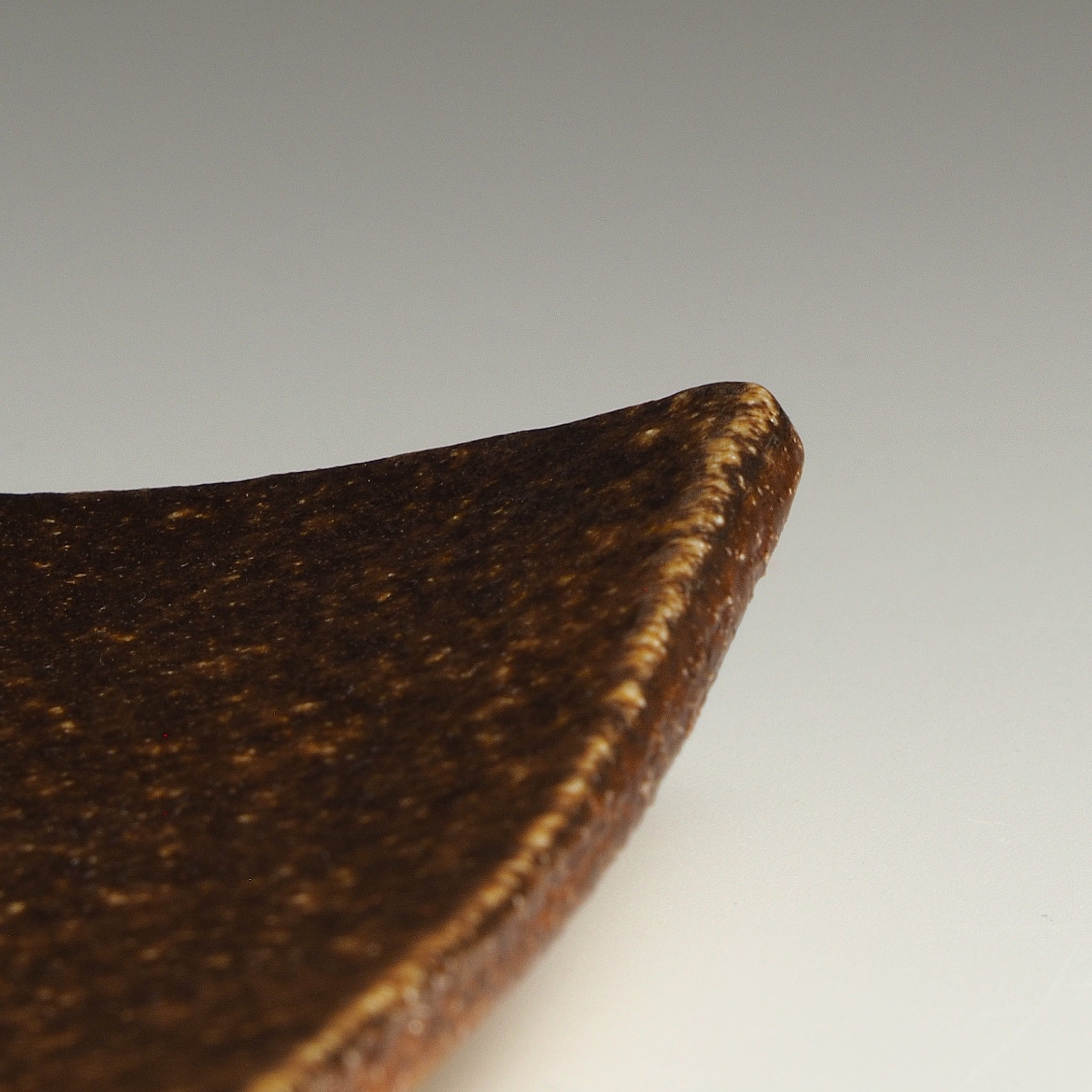 Close-up of the corner of the Nagafune handmade Shigaraki plate showing its warm brown surface and thin raised edge.
